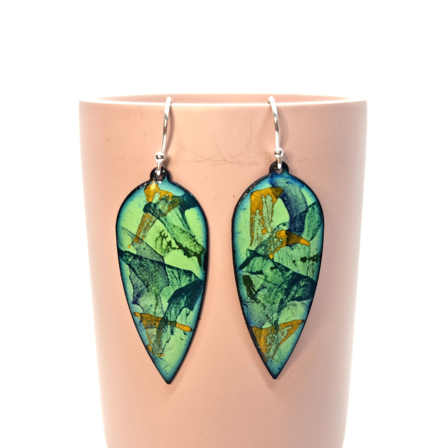 Large teardrop-shaped enamel drop earrings with splashes of dark blue, green and yellow on a light green background