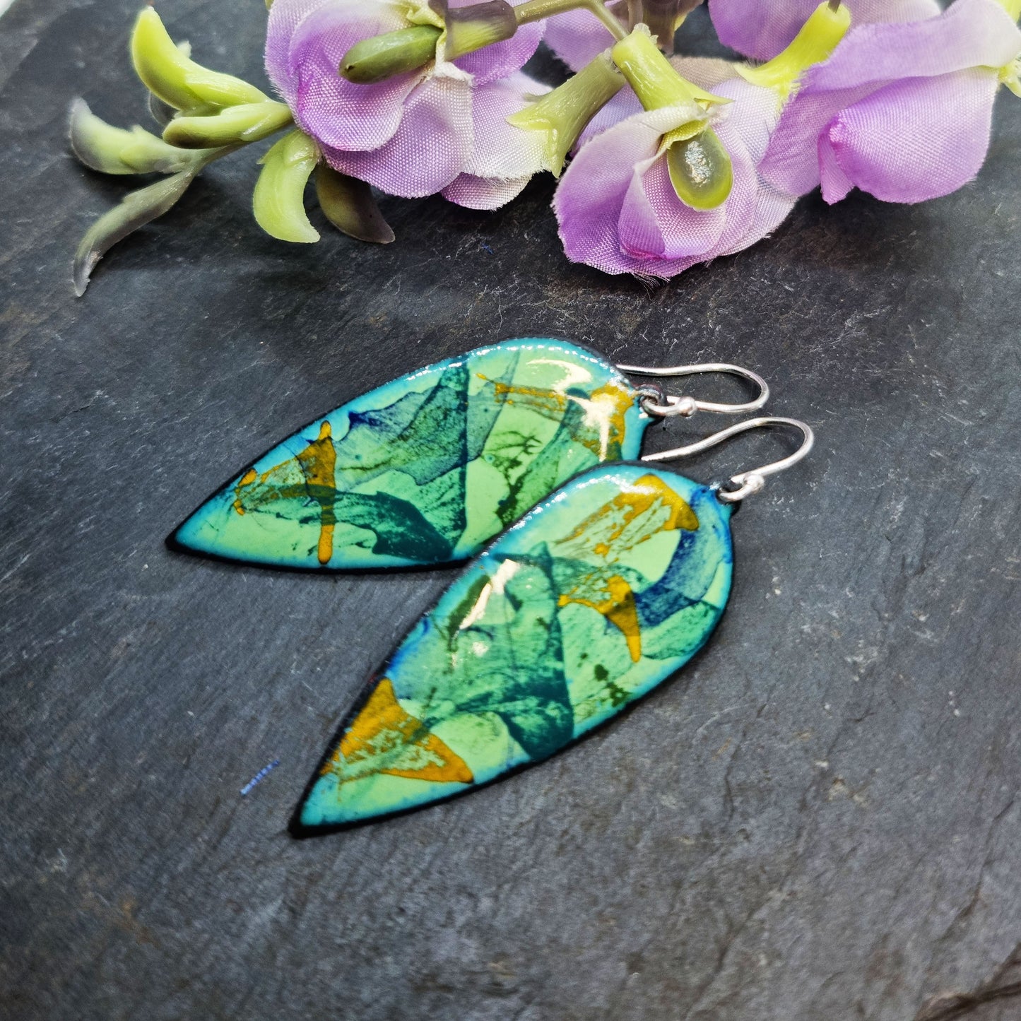 Large teardrop-shaped enamel drop earrings with splashes of dark blue, green and yellow on a light green background - with flowers