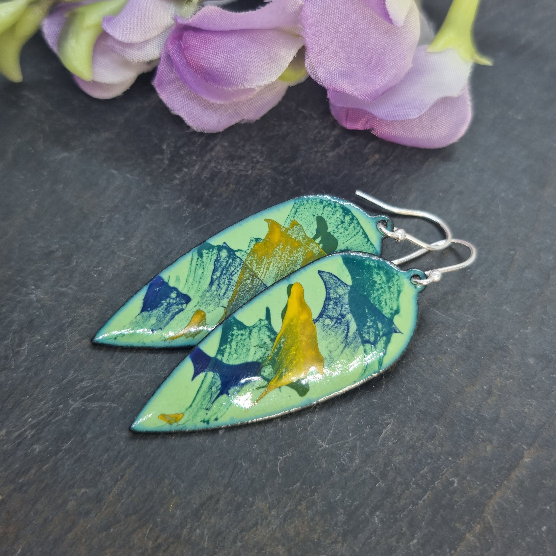 Large teardrop-shaped enamel drop earrings with splashes of dark blue, green and yellow on a light green background - with flowers