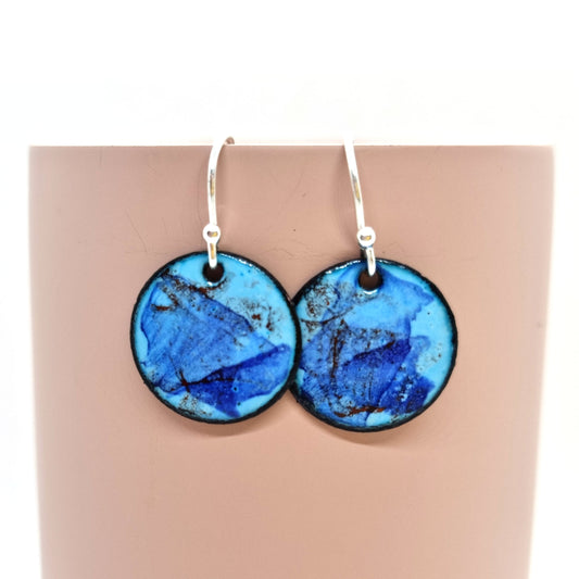 Round enamel drop earrings with splashes of dark blue and red on a light blue background.