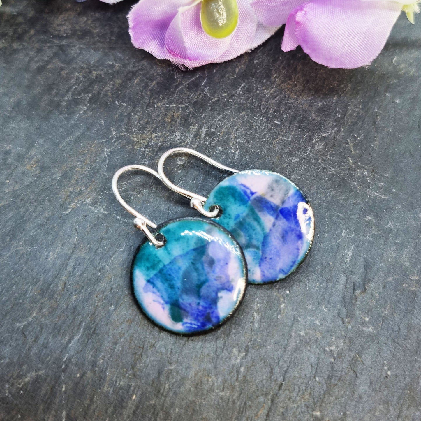 Round enamel drop earrings with splashes of dark blue, green and grey on a light purple background - with flowers