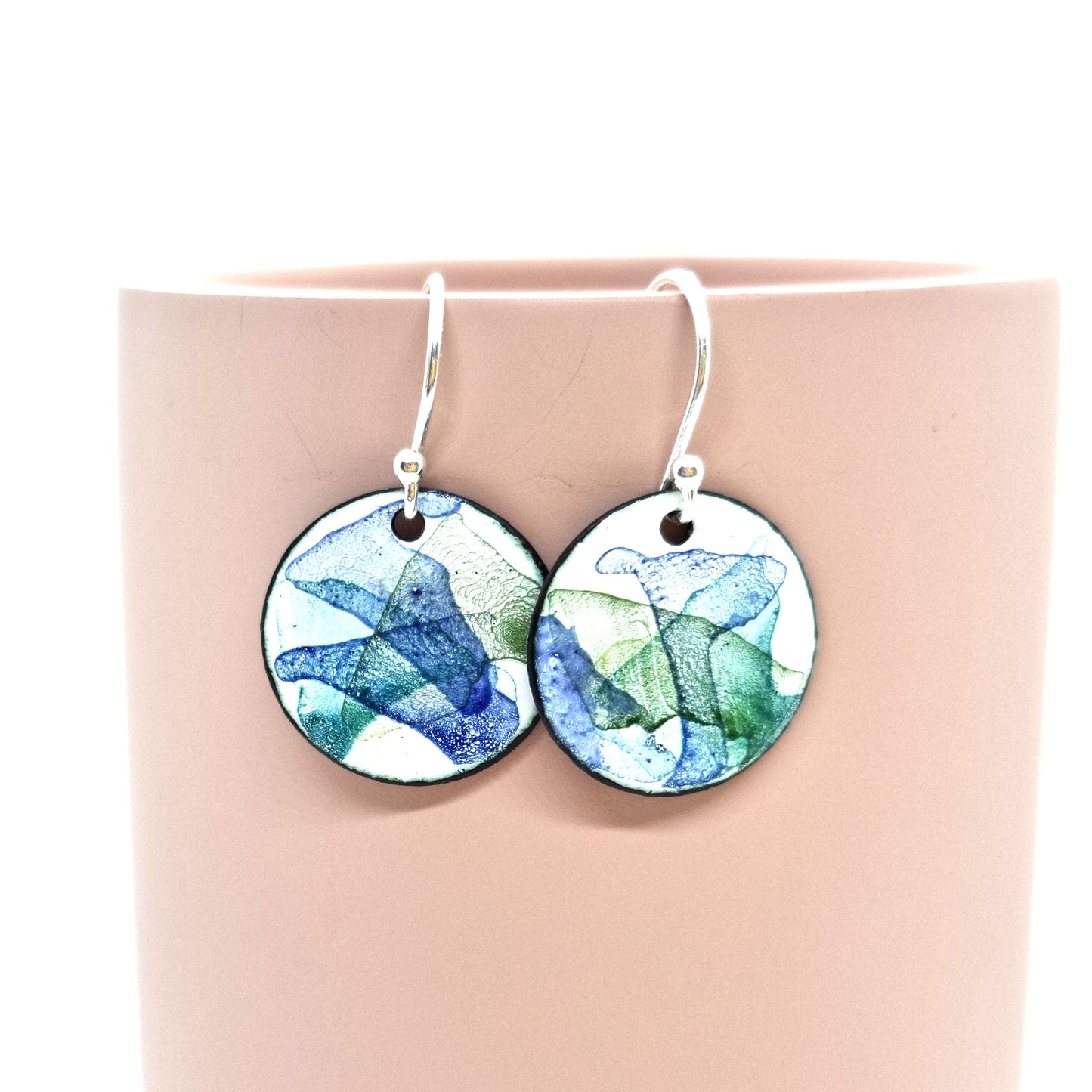 Round enamel drop earrings with splashes of dark blue and green on a white background.