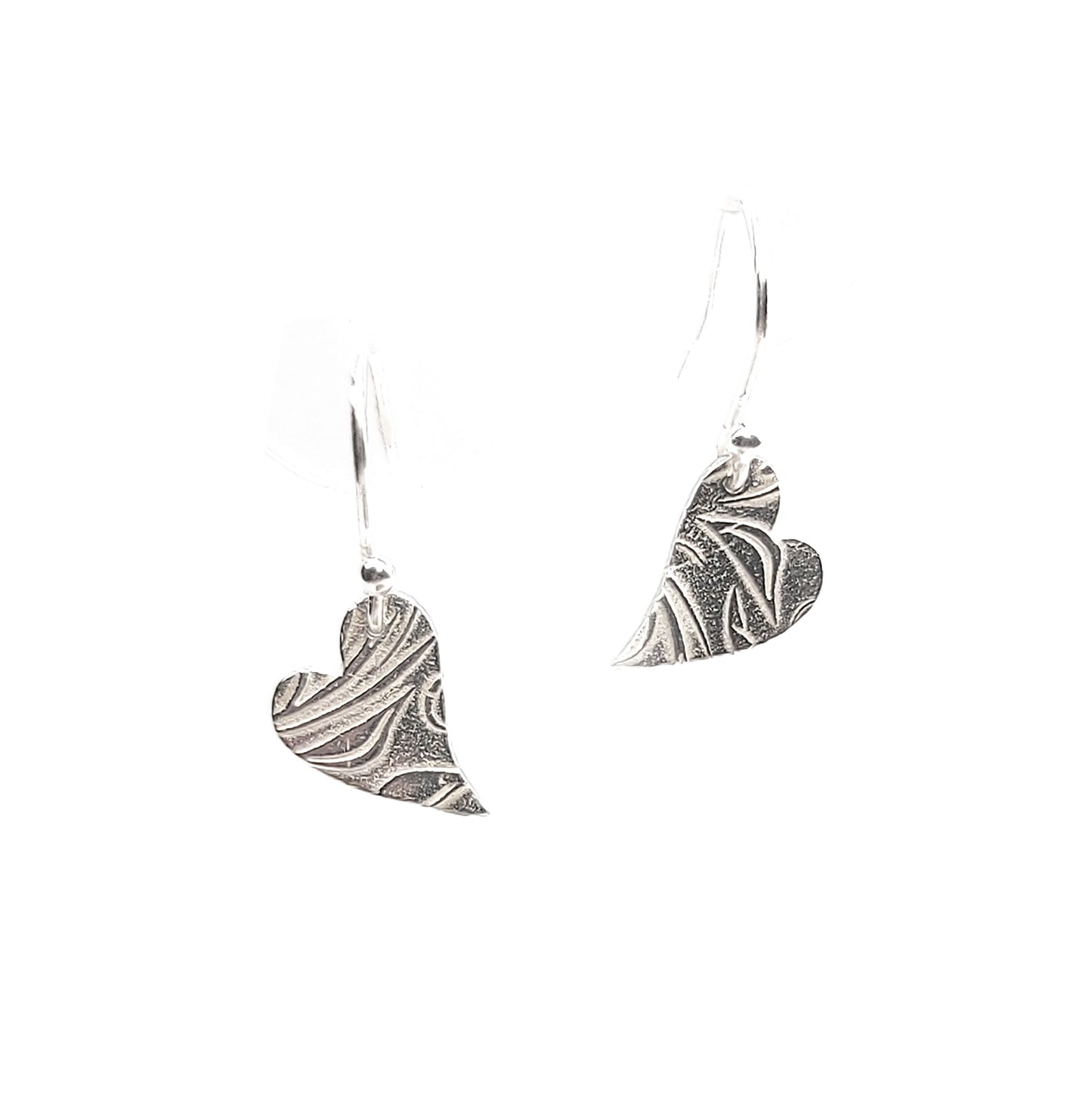 Silver heart drop earrings featuring an asymmetrical heart with a leaf and vine pattern suspended from silver ear hooks.