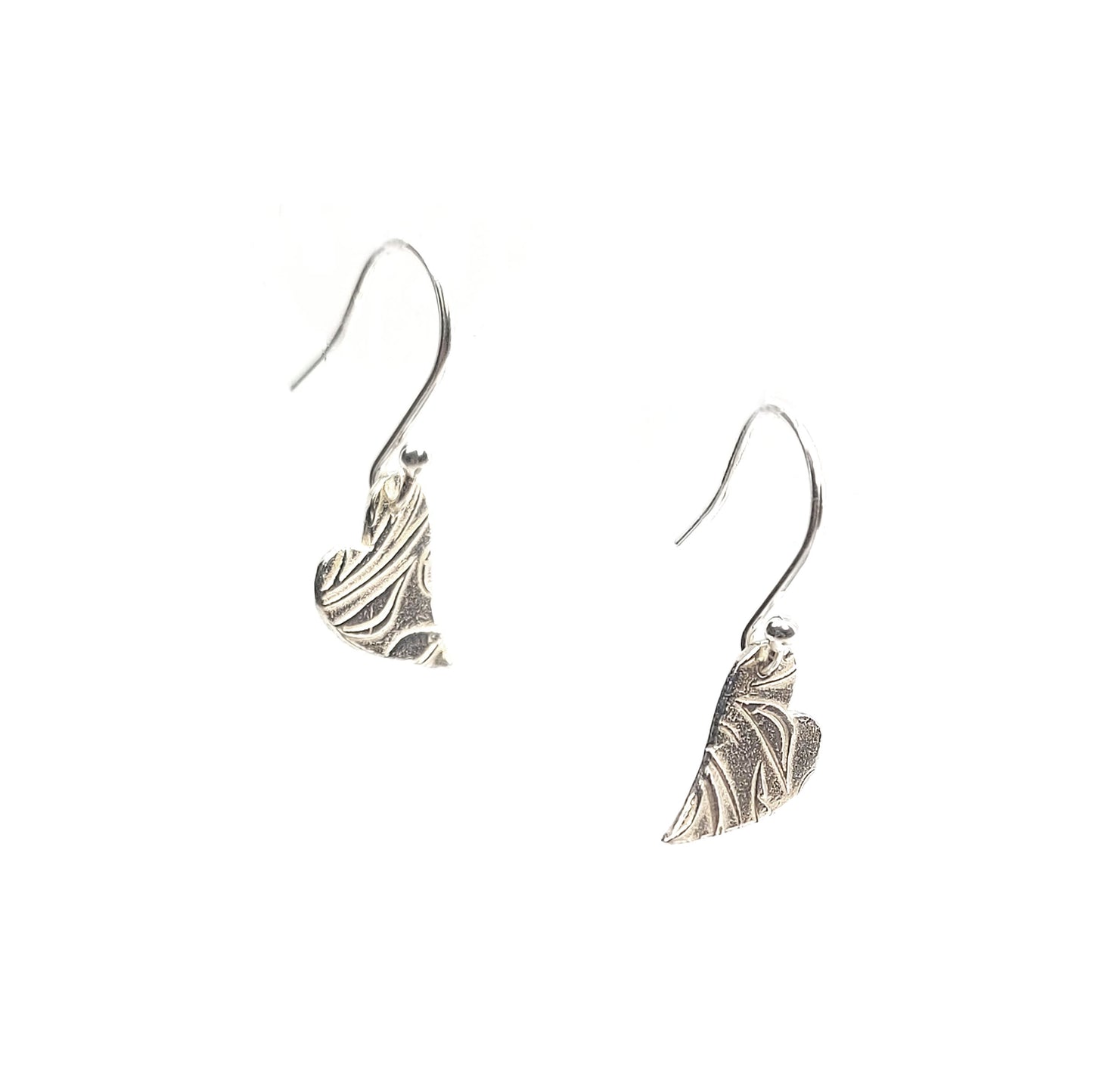 Silver heart drop earrings featuring an asymmetrical heart with a leaf and vine pattern suspended from silver ear hooks.