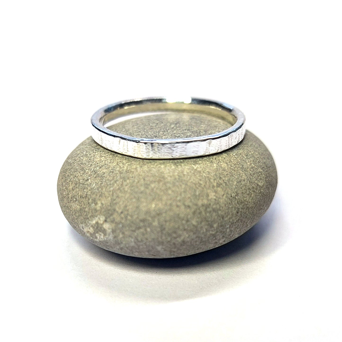 Silver band ring with line pattern sat on a pebble