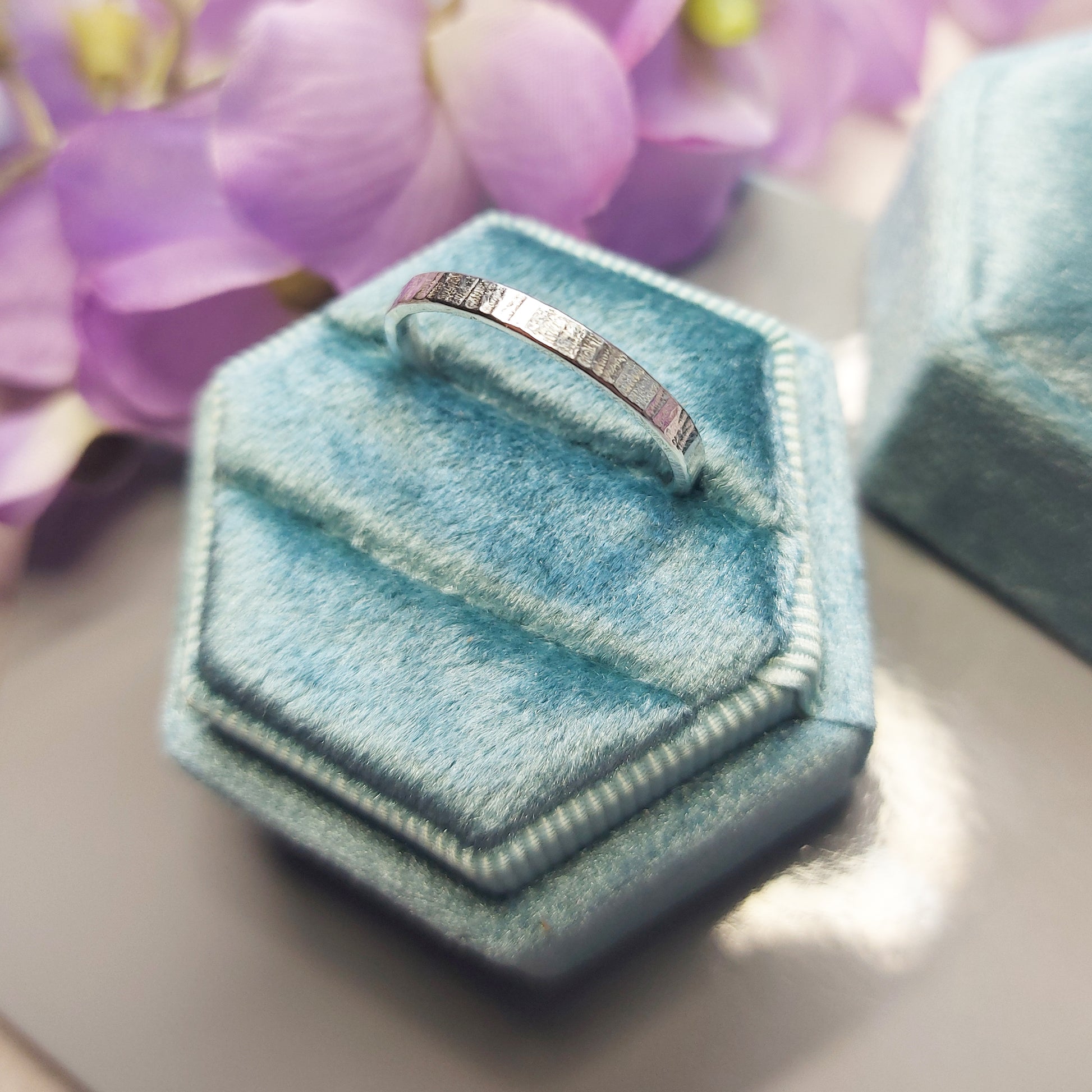 Silver band ring with line pattern in jewellery box with flowers