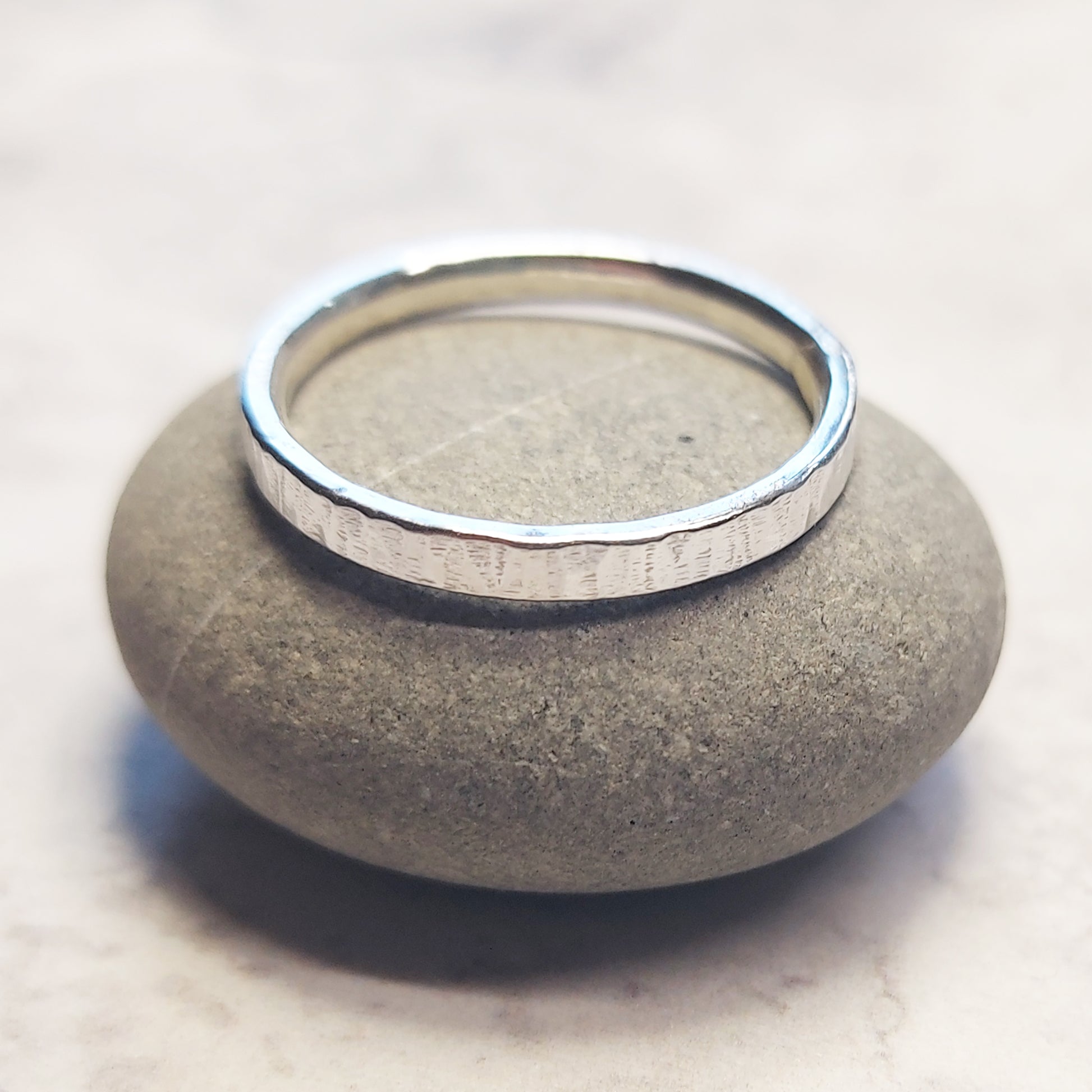 Silver band ring with line pattern sat on a pebble