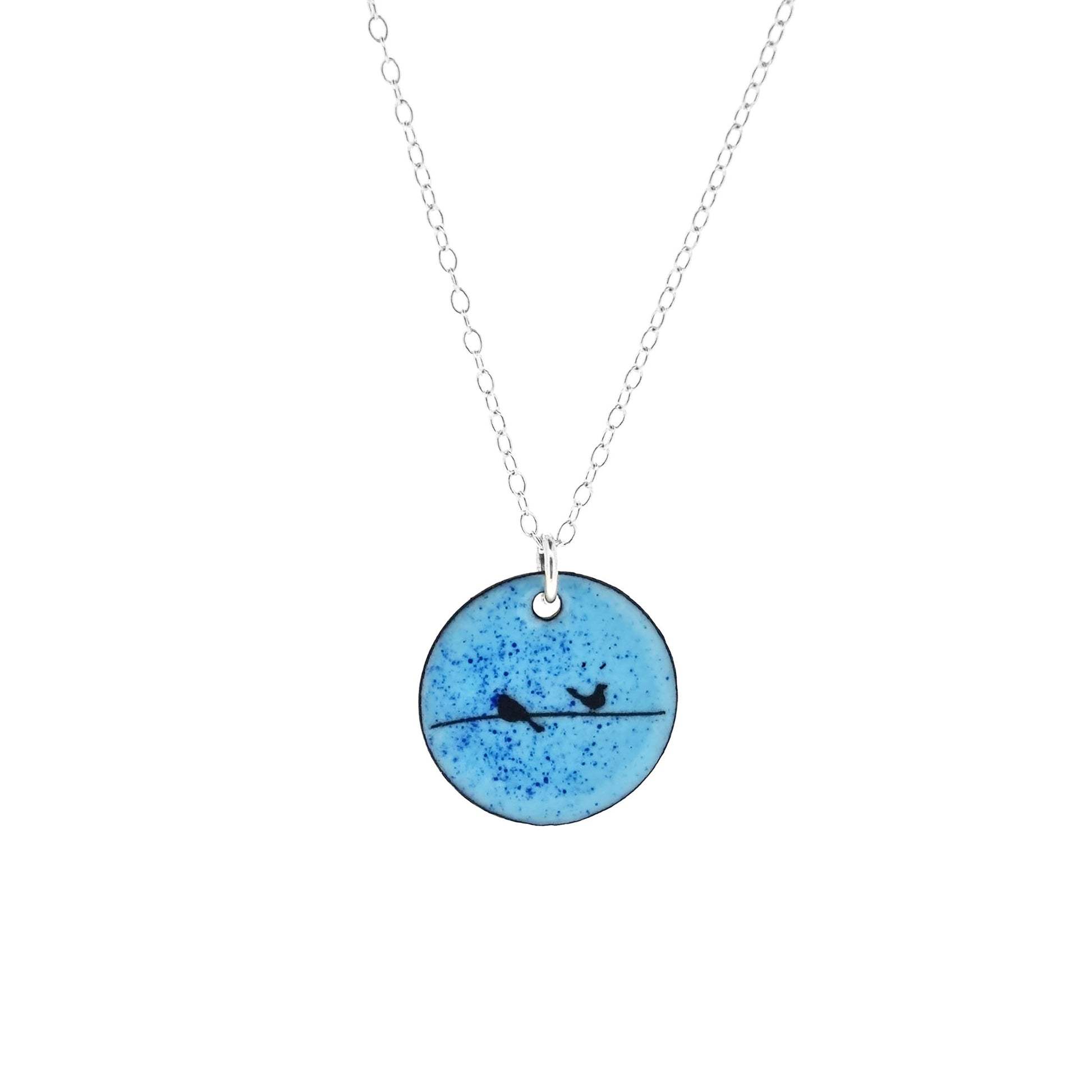 Round enamel pendant with bird silhouettes sat on a wire against a blue background. Suspended on a silver chain.