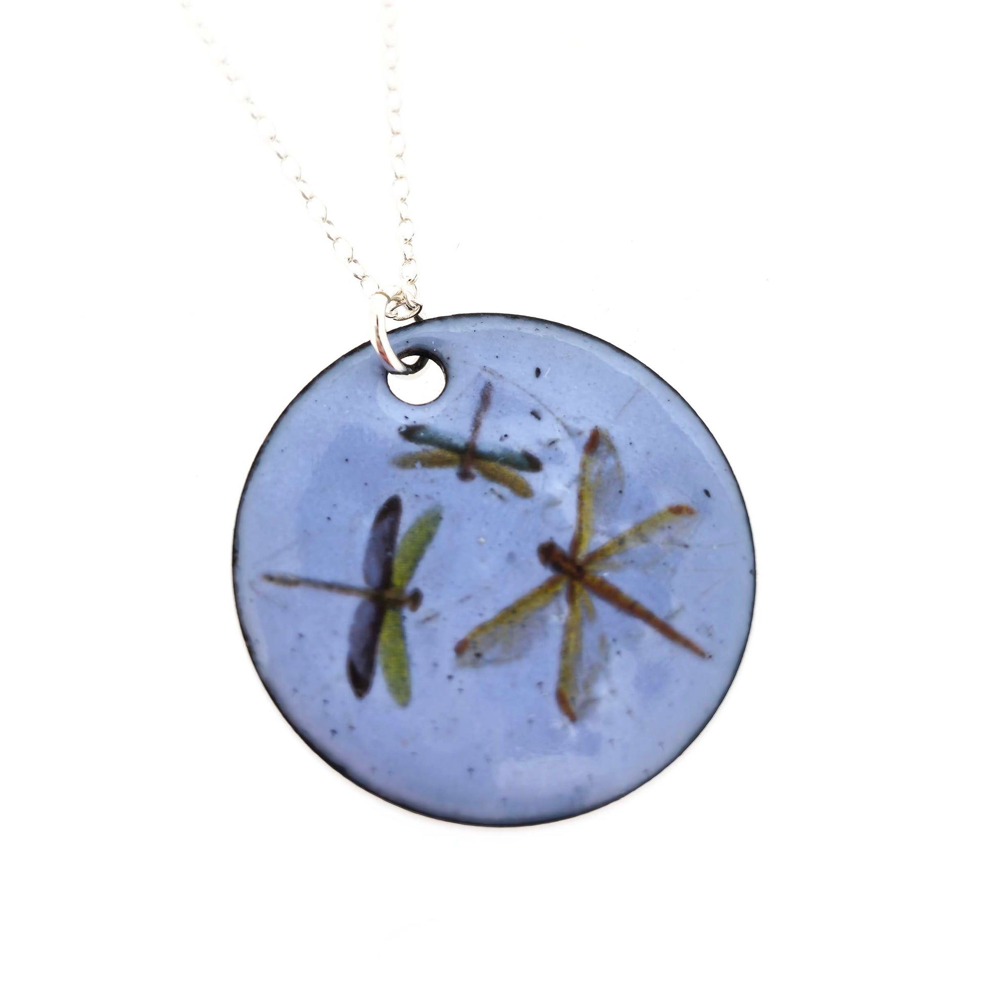 Round enamel pendant with dragonfly designs on a pastel blue background with a silver chain. On a white background.