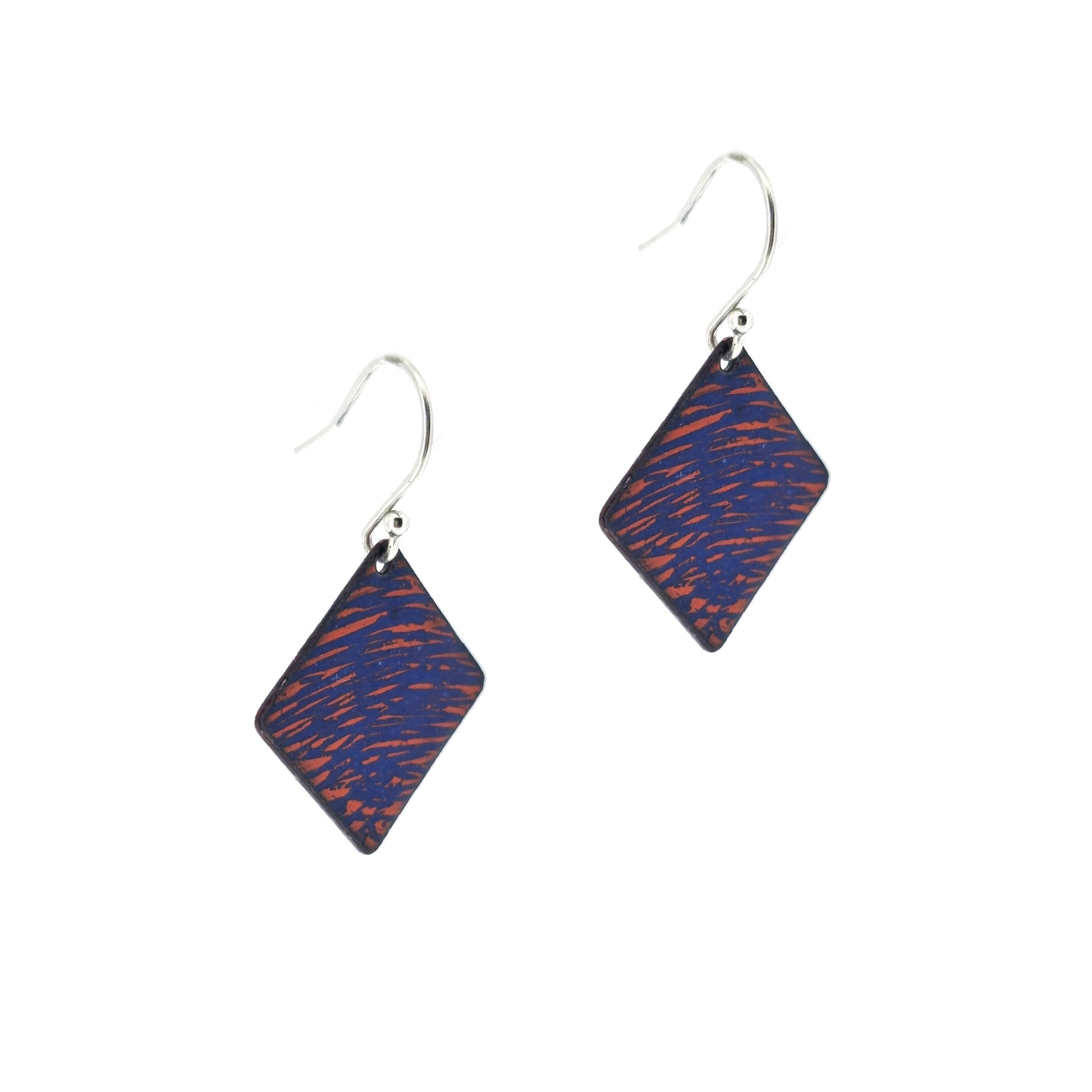 Square (diamond shaped) drop earrings with a rustic line pattern of dark blue and orange enamel. On silver ear hooks. Side view.