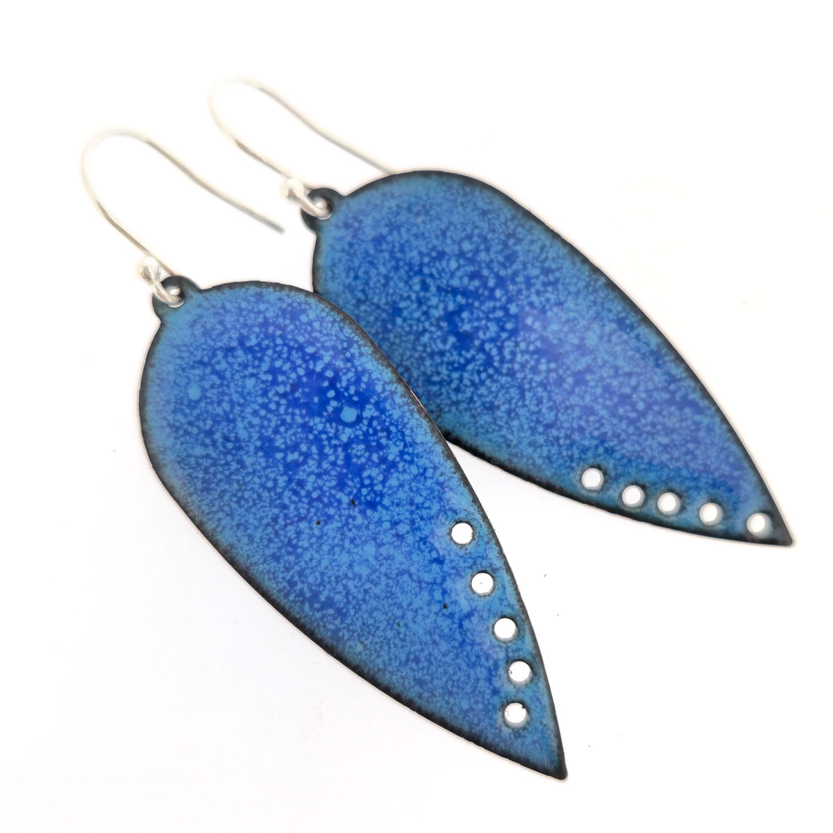 A pair of handmade teardrop-shaped blue enamel dangle earrings with silver fishhook wires and small circle cutouts along the lower edge, shown against a plain white background. Mijoux jewellery.