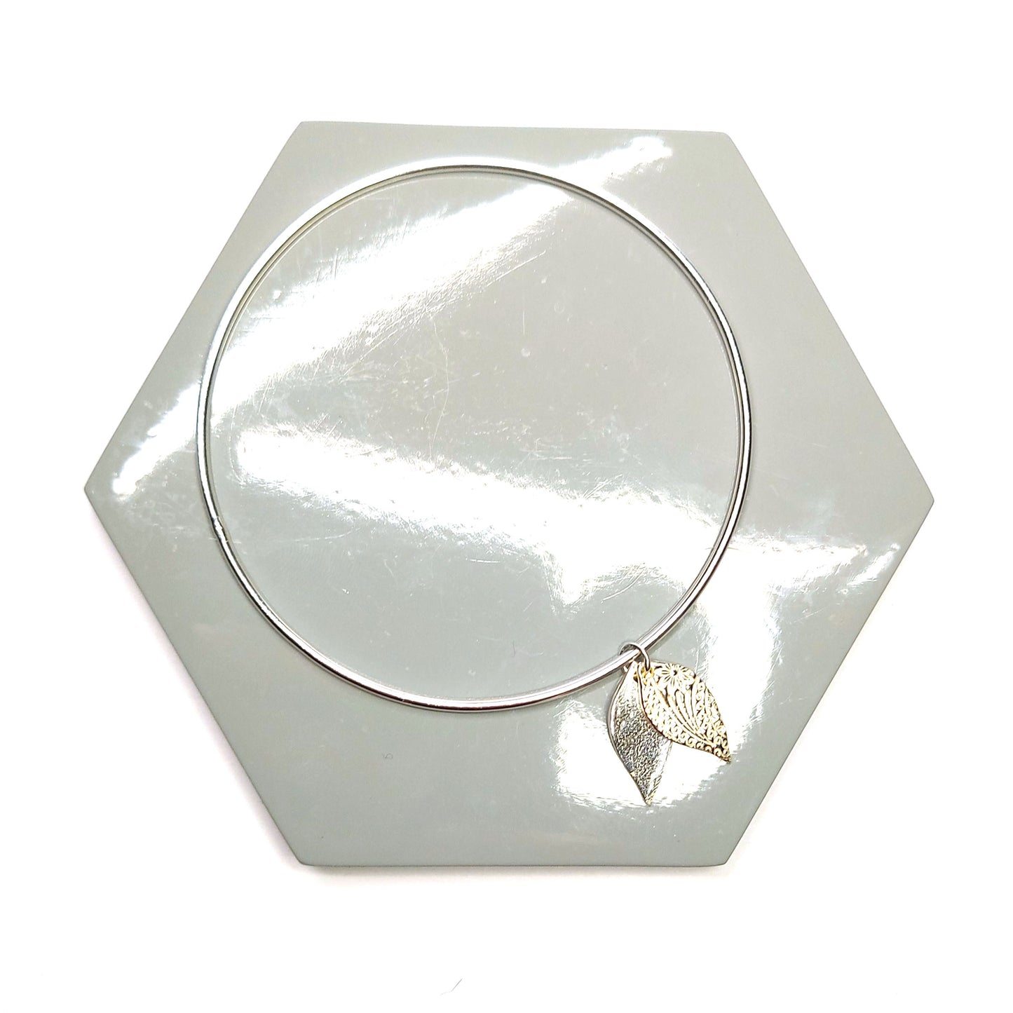 A round silver bangle with a double leaf-shaped patterned charm.