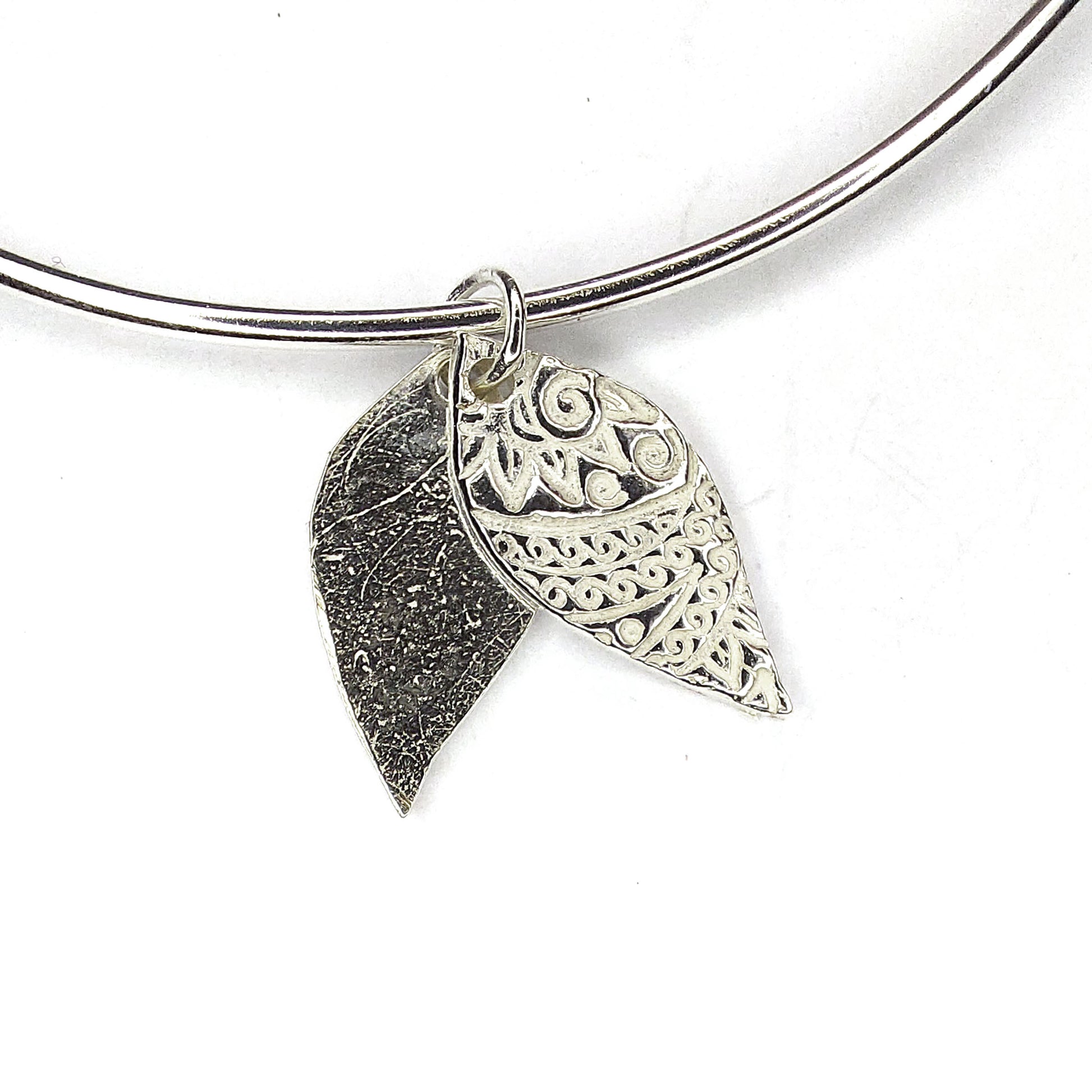 A rClose up of the double leaf-shaped patterned charm on a bangle.