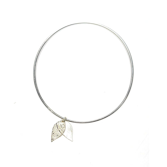 A round silver bangle with a double leaf-shaped patterned charm.