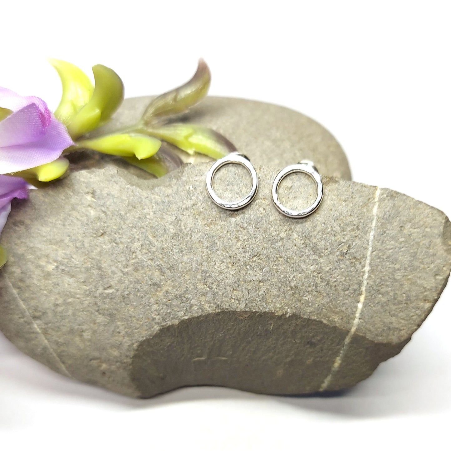 Sterling silver open circle stud earrings on pebble with flowers.