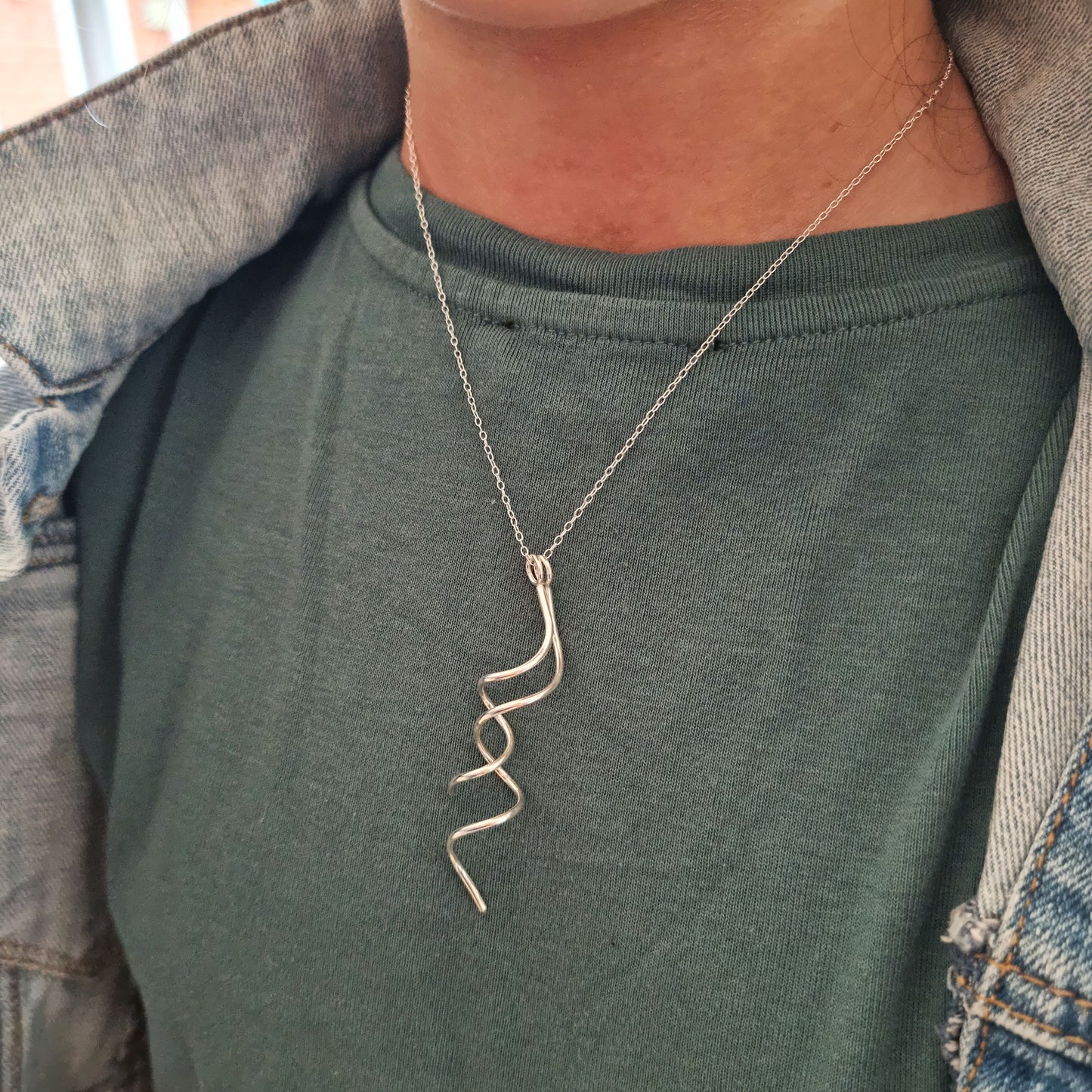 A silver twist pendant with 2 strands intertwined suspended from a silver chain. Pictured being worn.