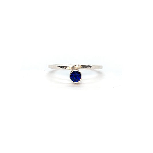 A silver thin ring with a hammered finish. The ring has a dark blue sapphire bezel set alongside a silver dot.