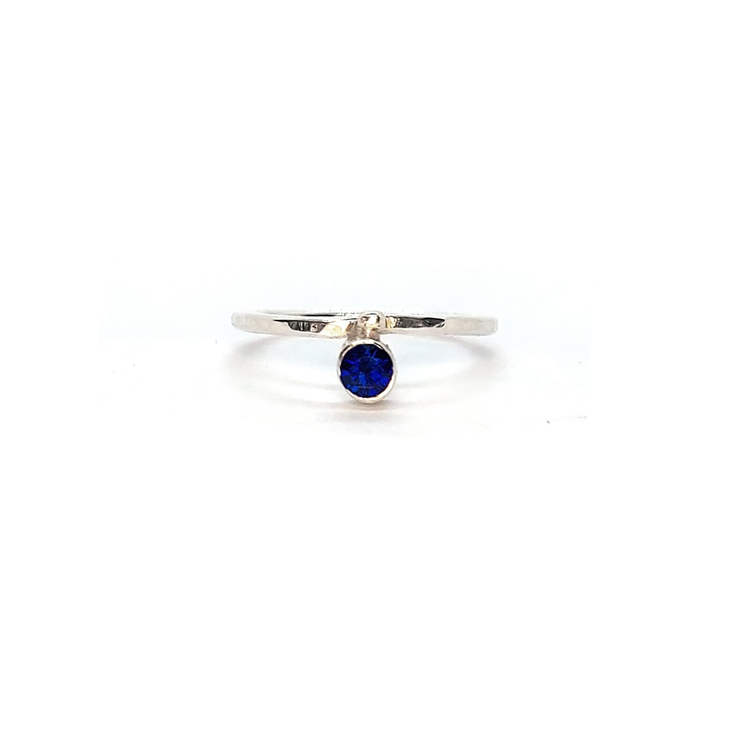 A silver thin ring with a hammered finish. The ring has a dark blue sapphire bezel set alongside a silver dot.