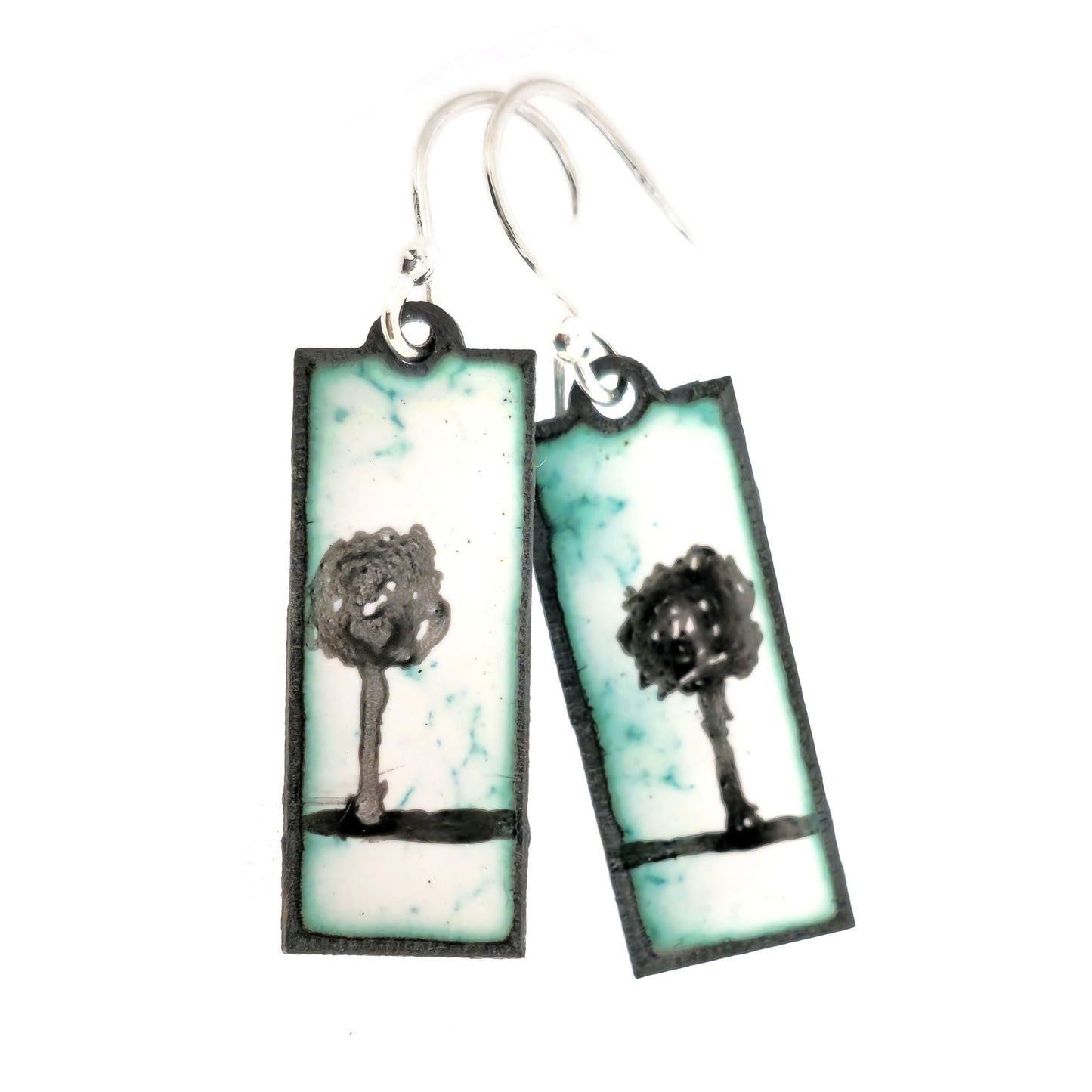 Rectangle enamel earrings with a single tree silhouette on each earring, in white, green and black, suspended from silver hooks.On a white background. Handmade. Mijoux Jewellery.