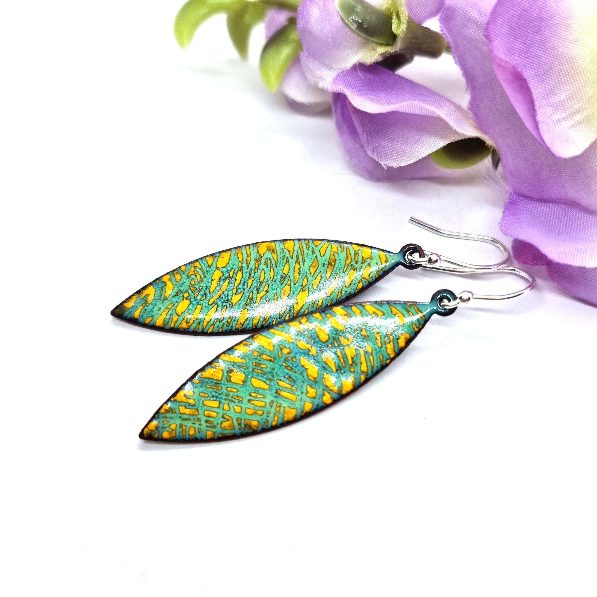 Boat shaped drop earrings with a rustic line pattern of light green and yellow enamel. With silver ear hooks. Pictured with flower.