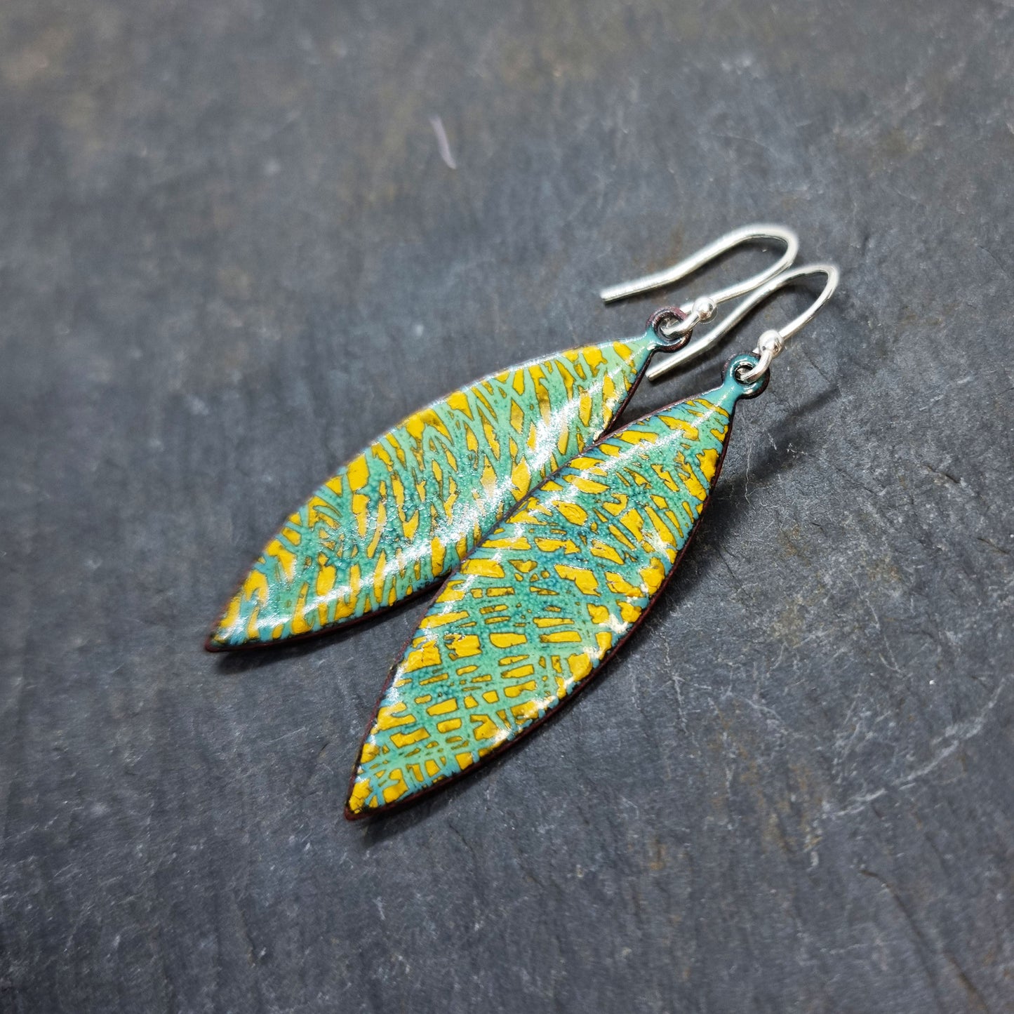 Boat shaped drop earrings with a rustic line pattern of light green and yellow enamel. With silver ear hooks.