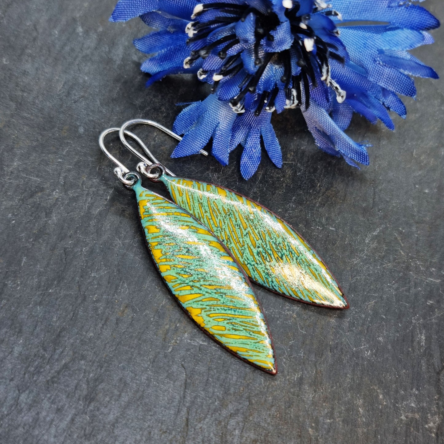 Boat shaped drop earrings with a rustic line pattern of light green and yellow enamel. With silver ear hooks. Pictured with flower.