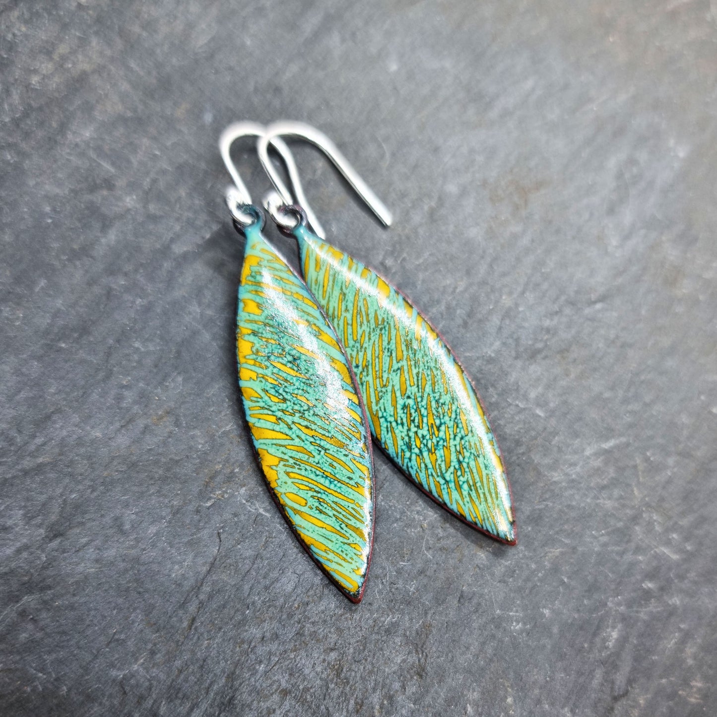 Boat shaped drop earrings with a rustic line pattern of light green and yellow enamel. With silver ear hooks.