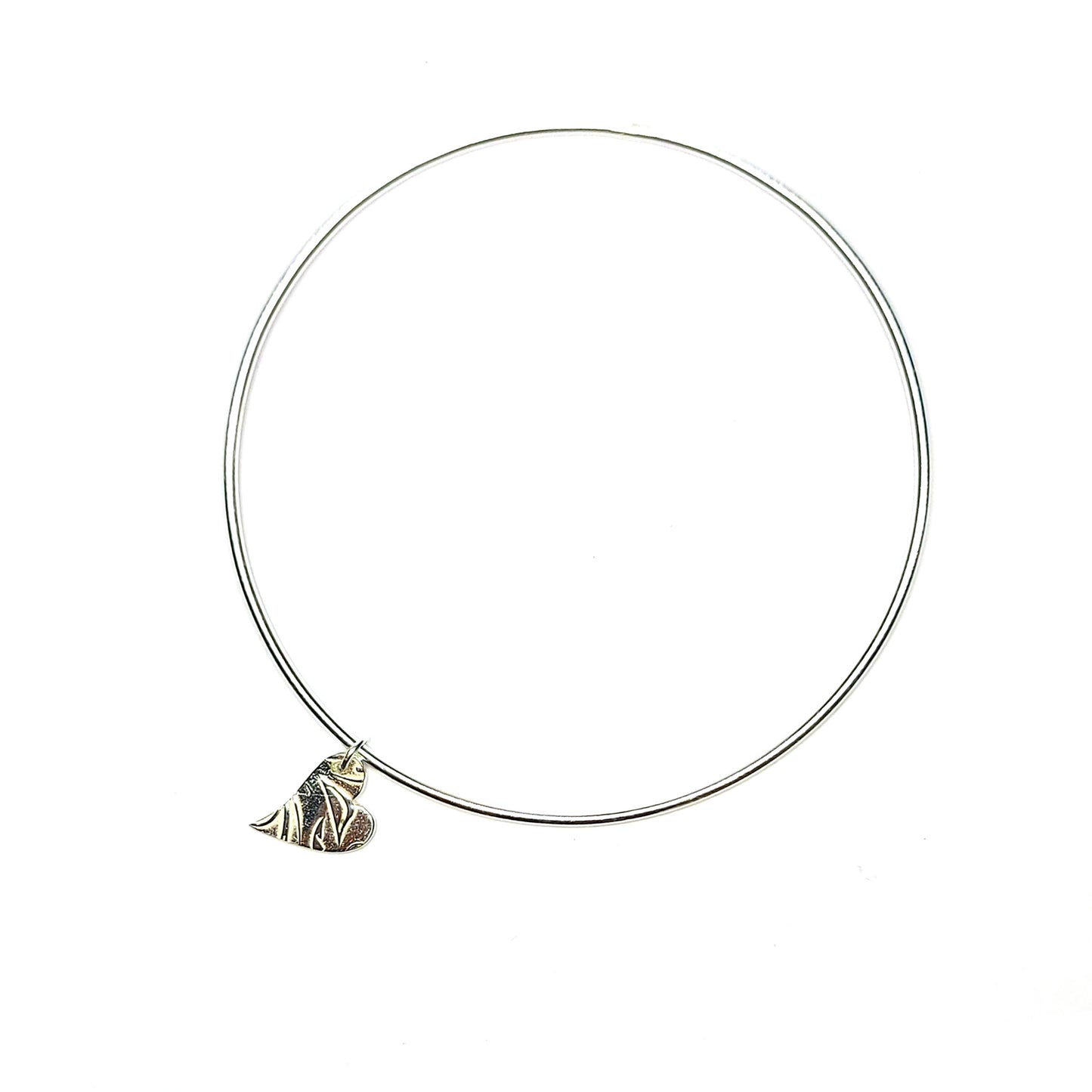 A round silver bangle with an asymmetrical patterned heart charm.