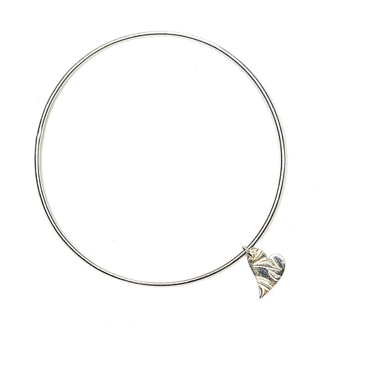 A round silver bangle with an asymmetrical patterned heart charm.