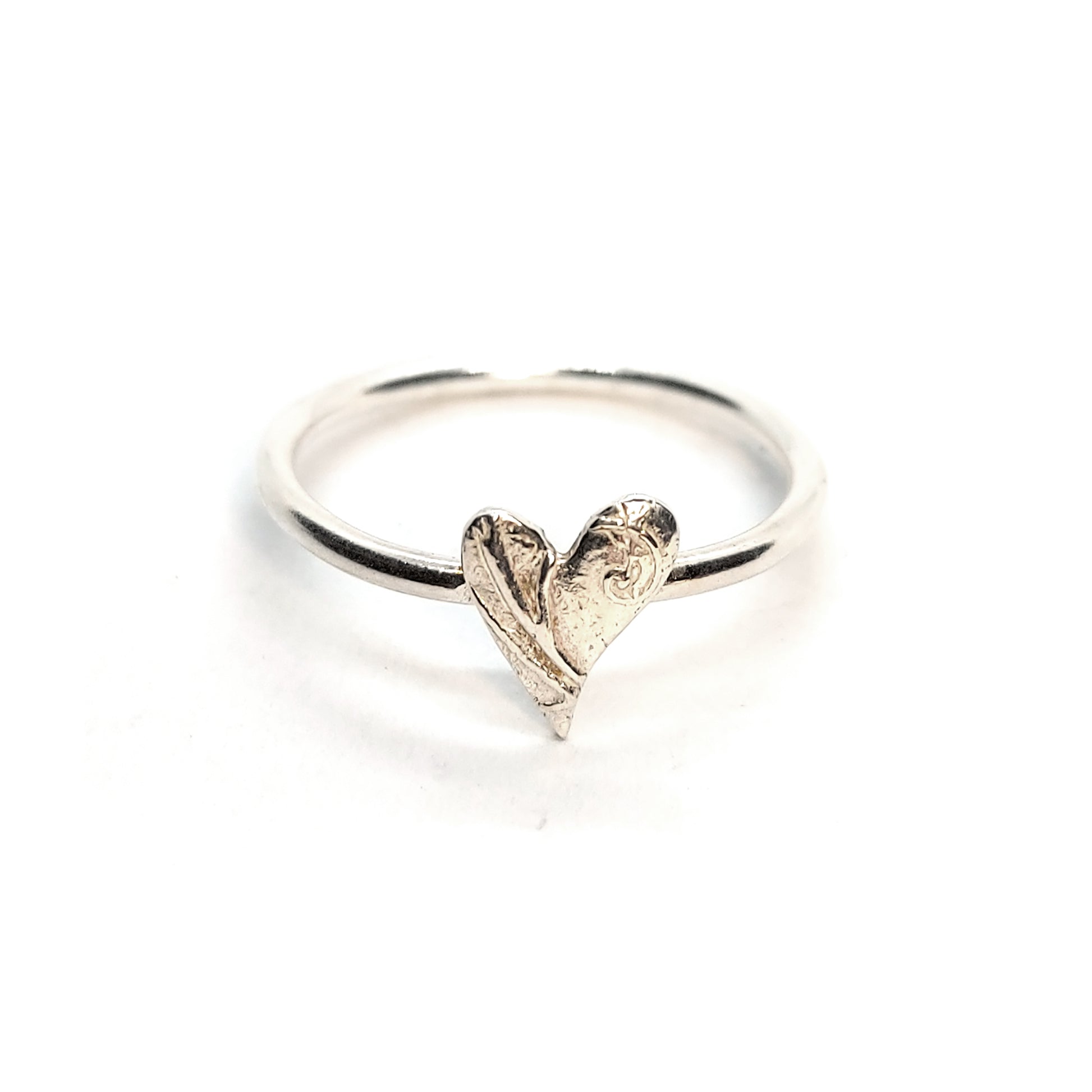 A silver stacking ring with an asymmetric patterned heart in the centre.