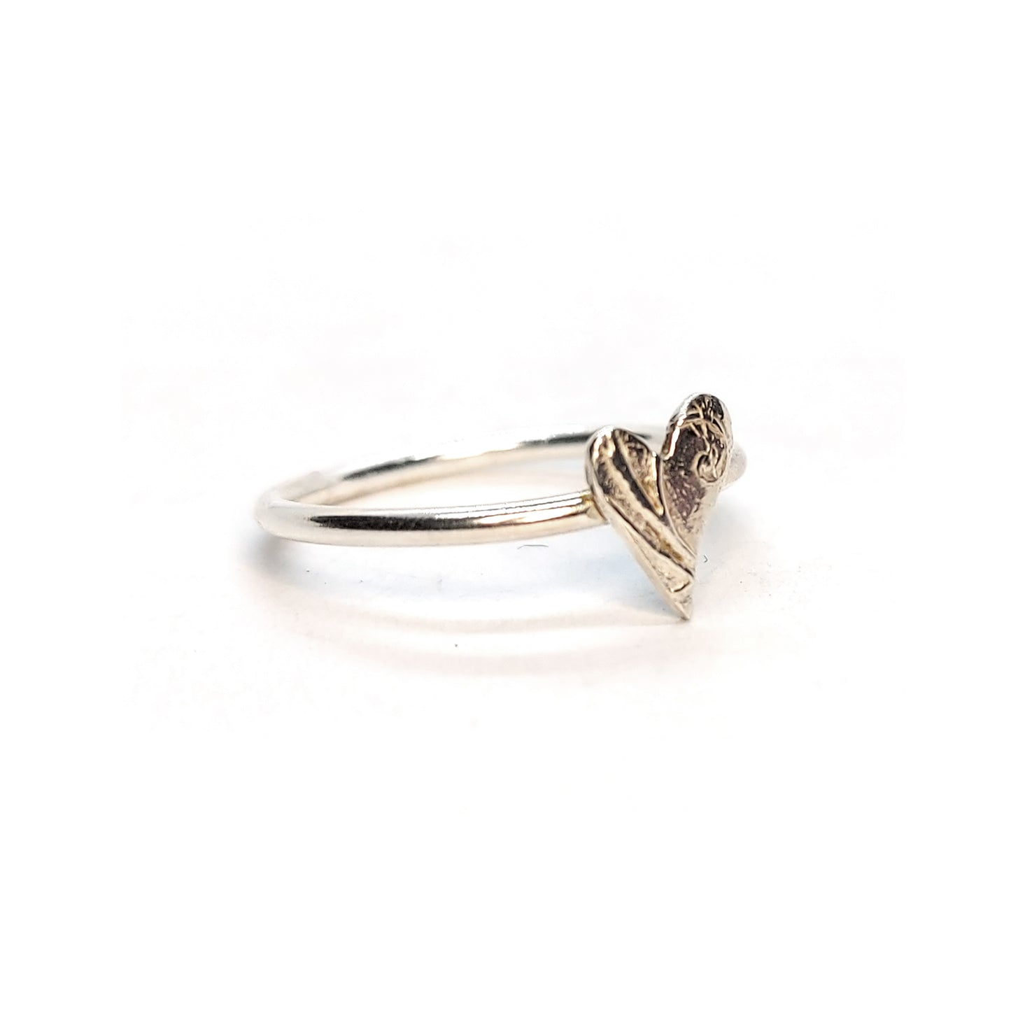 A silver stacking ring with an asymmetric patterned heart in the centre.