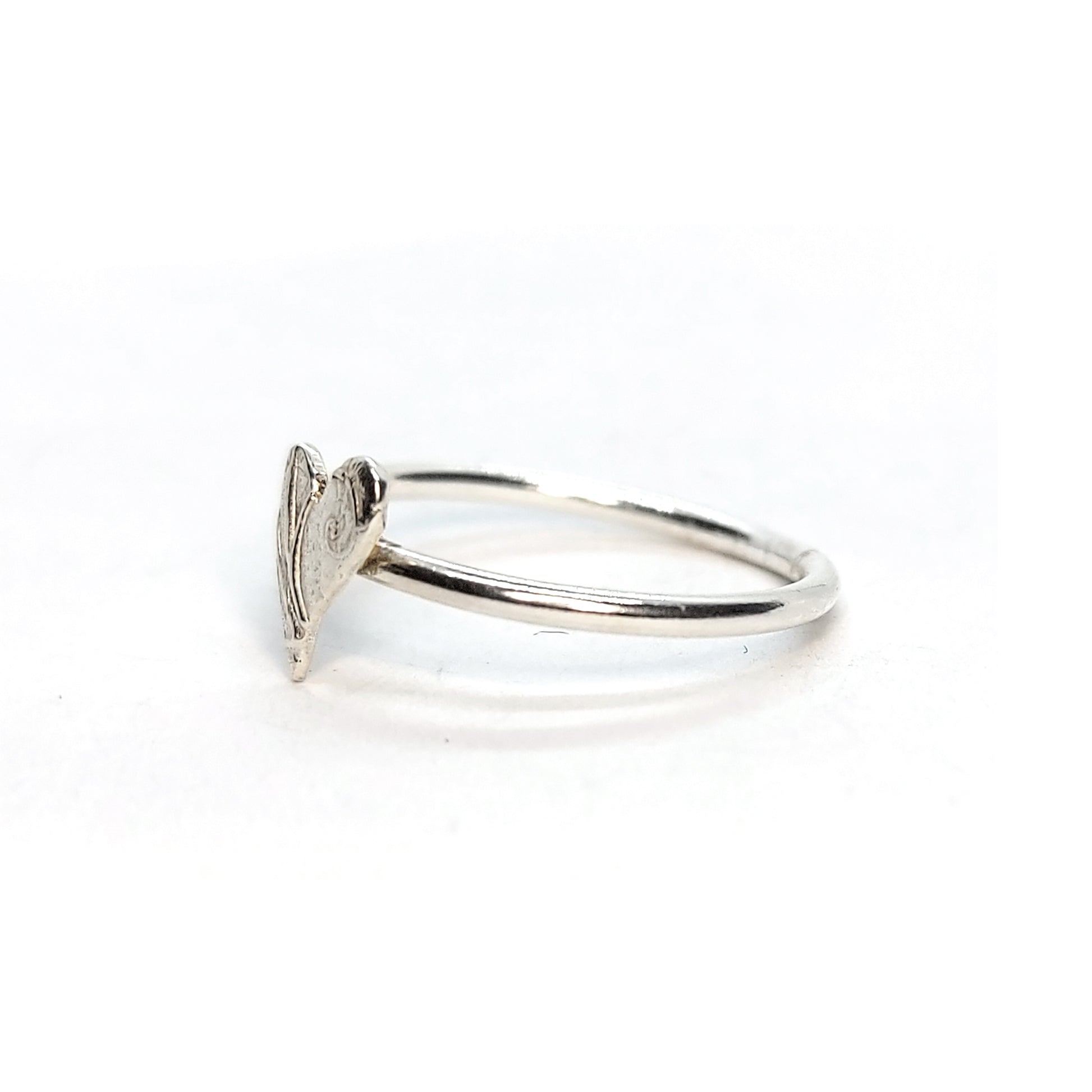 A silver stacking ring with an asymmetric patterned heart in the centre.