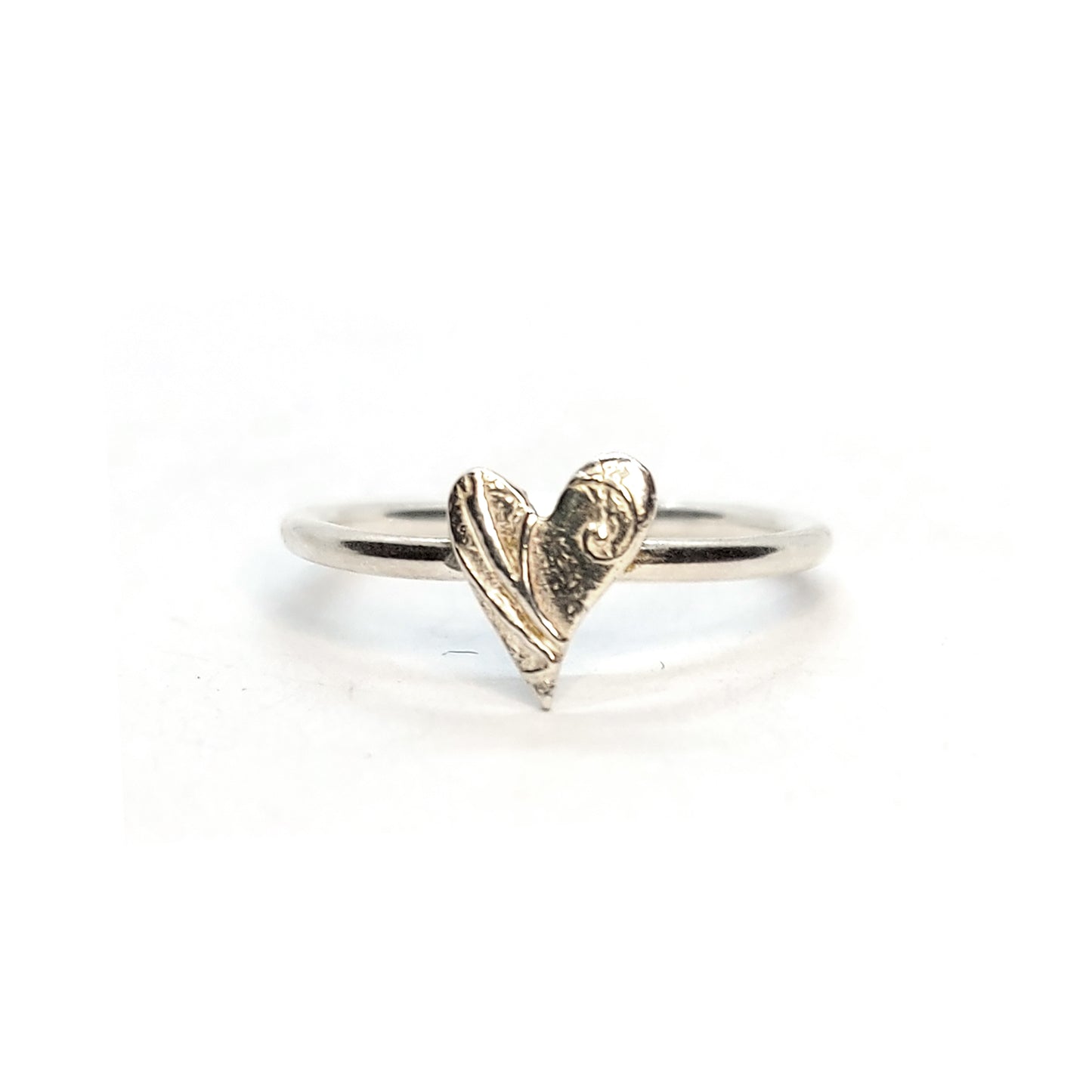 A silver stacking ring with an asymmetric patterned heart in the centre.
