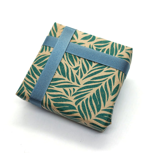 A wrapped box with leaf pattern brown and green wrapping paper and grey ribbon.