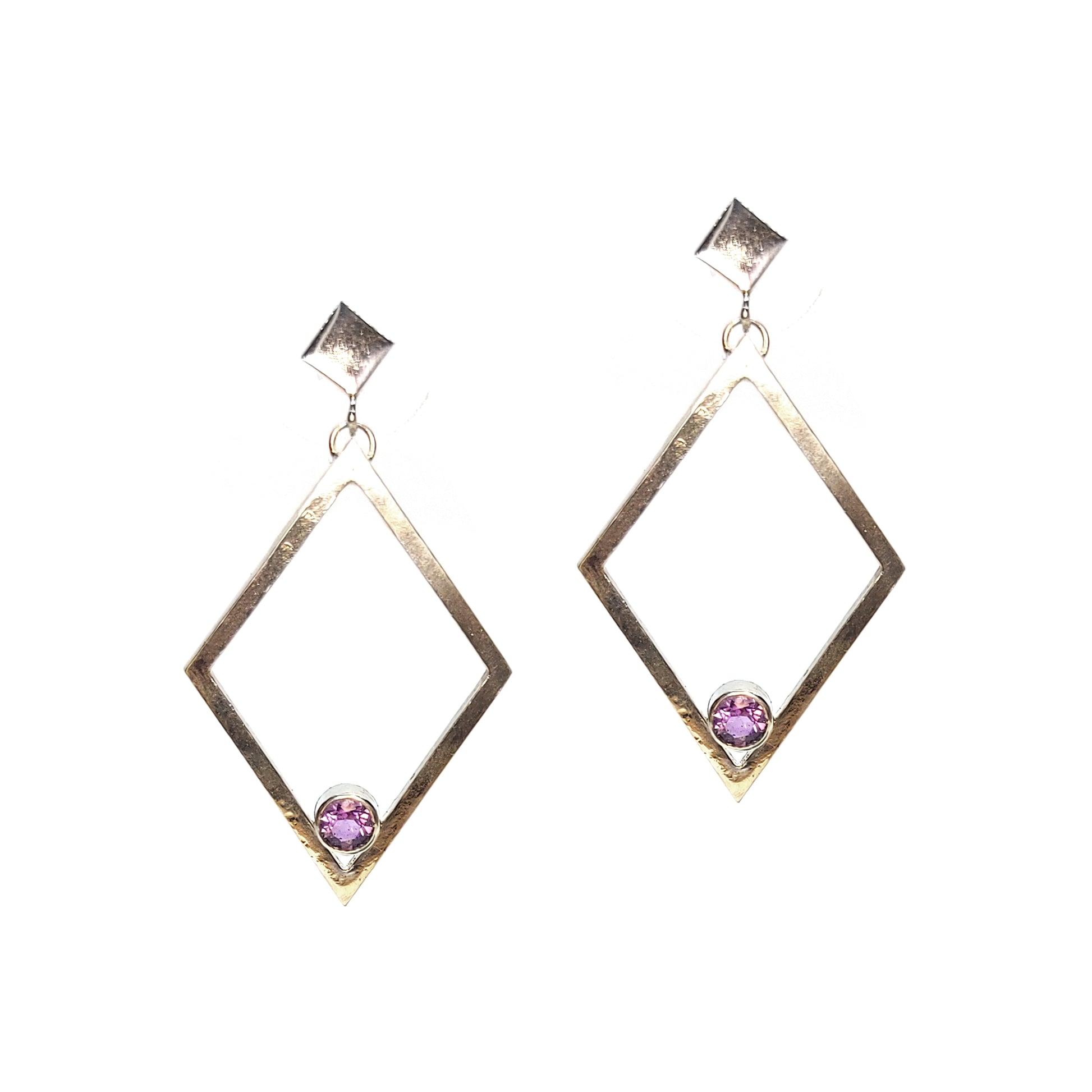 A pair of silver statement earrings featuring a top diamond shaped stud with a large open diamond shape drop beneath. Inside at the bottom of the large drop diamond is a round purple amethyst.