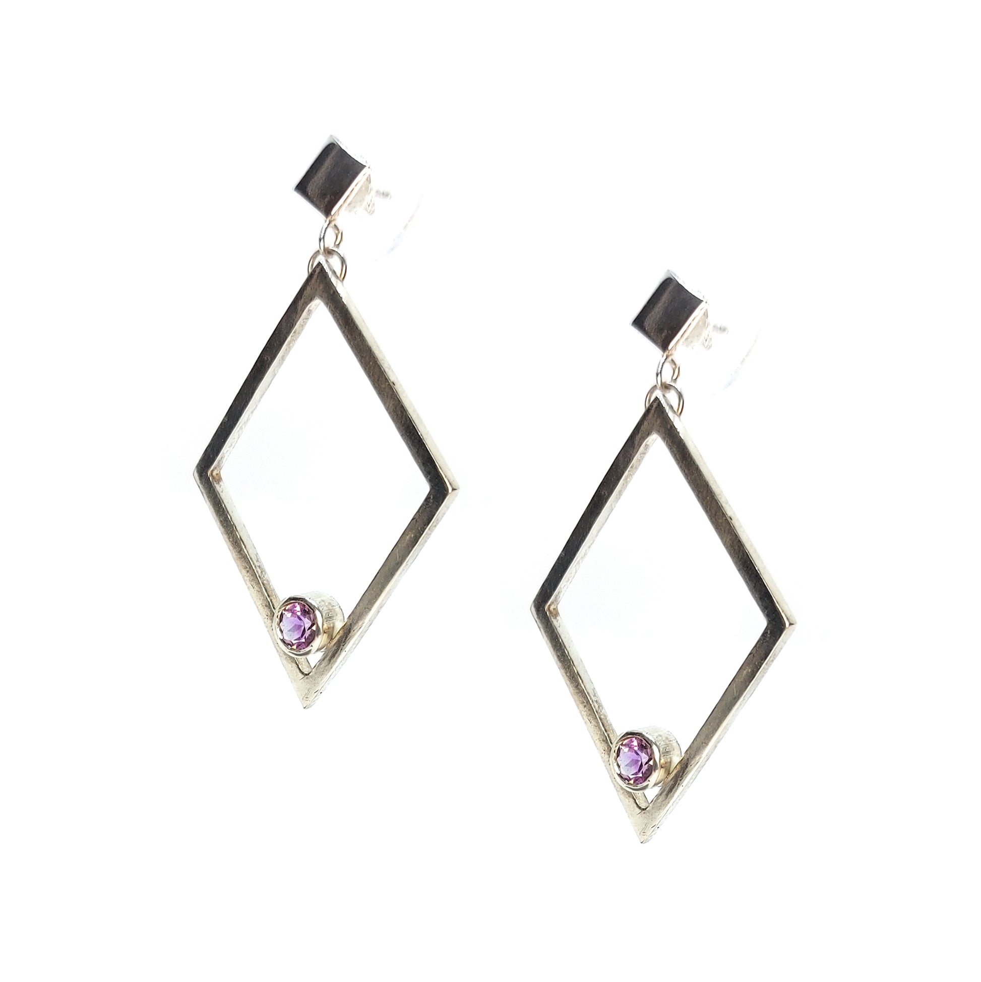 A pair of silver statement earrings featuring a top diamond shaped stud with a large open diamond shape drop beneath. Inside at the bottom of the large drop diamond is a round purple amethyst.