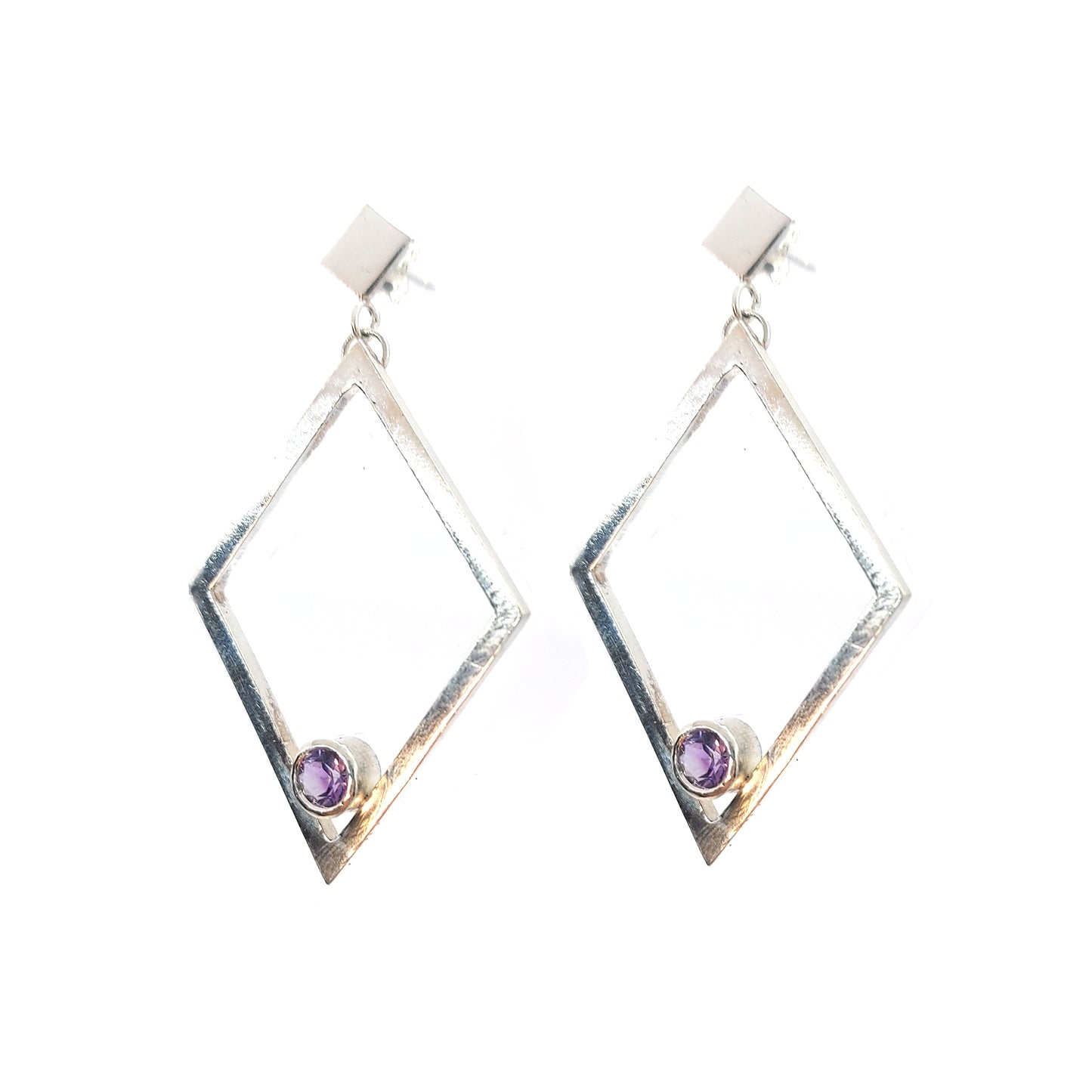 A pair of silver statement earrings featuring a top diamond shaped stud with a large open diamond shape drop beneath. Inside at the bottom of the large drop diamond is a round purple amethyst.