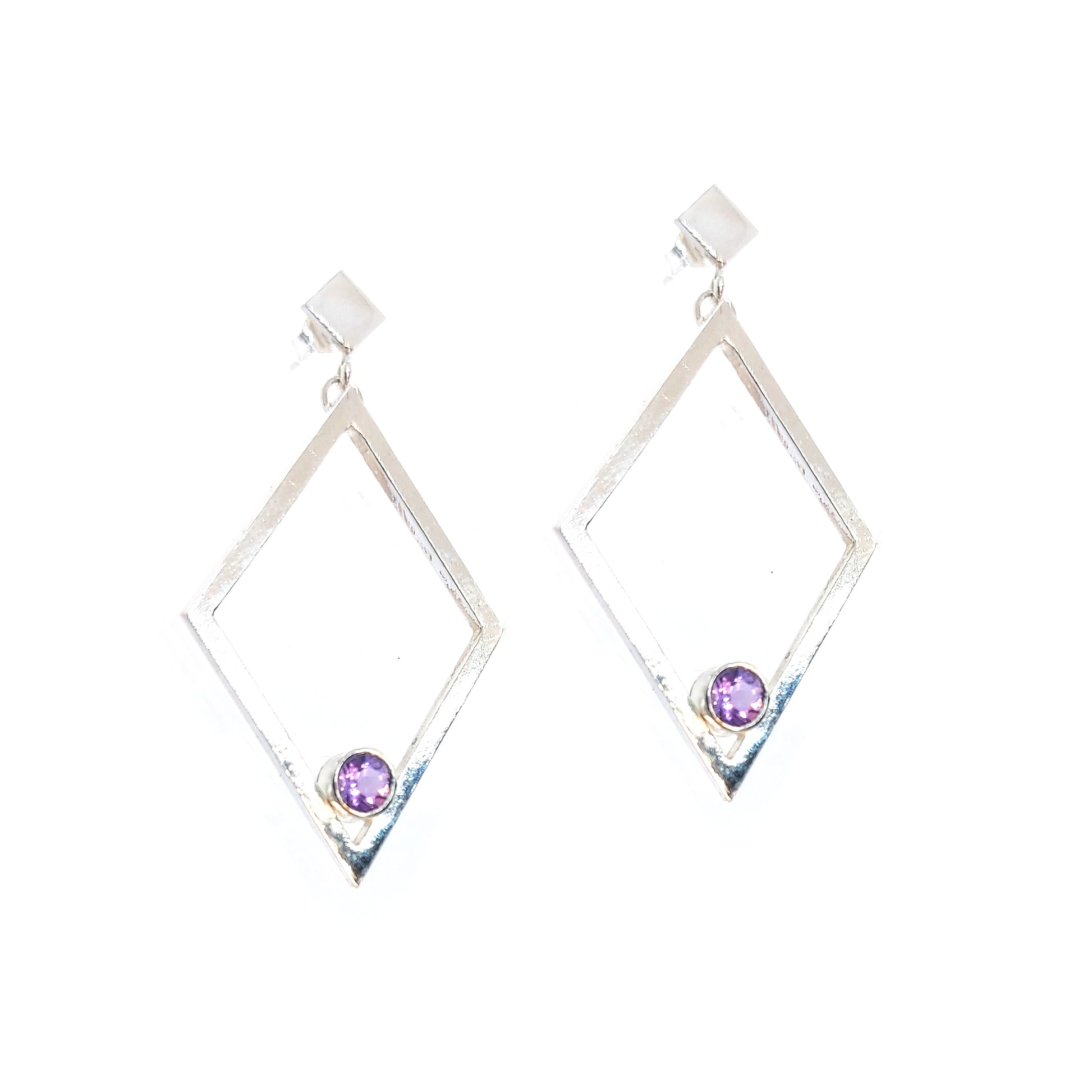 A pair of silver statement earrings featuring a top diamond shaped stud with a large open diamond shape drop beneath. Inside at the bottom of the large drop diamond is a round purple amethyst.