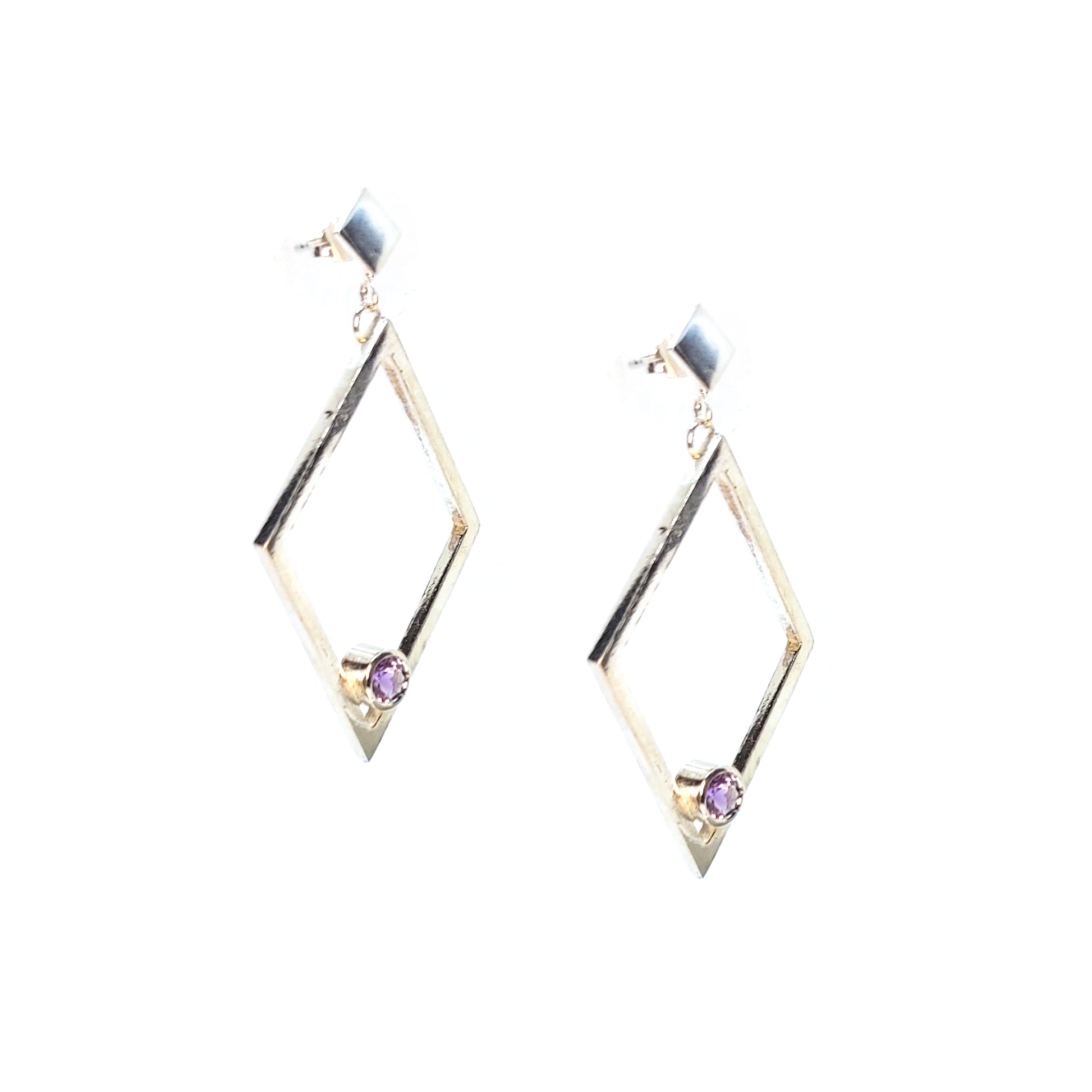 A pair of silver statement earrings featuring a top diamond shaped stud with a large open diamond shape drop beneath. Inside at the bottom of the large drop diamond is a round purple amethyst.