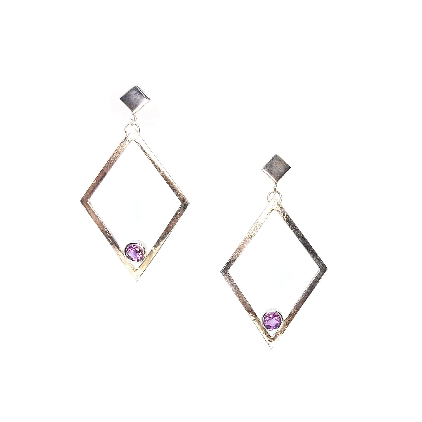 A pair of silver statement earrings featuring a top diamond shaped stud with a large open diamond shape drop beneath. Inside at the bottom of the large drop diamond is a round purple amethyst.