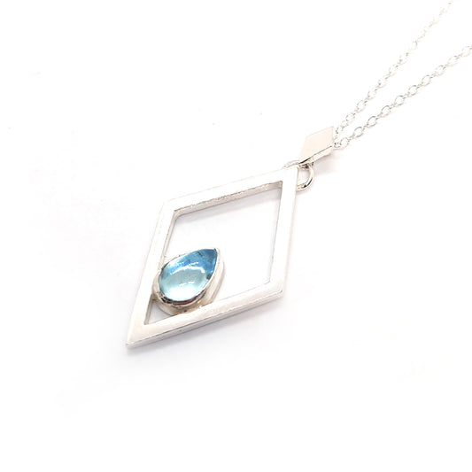 A silver open diamond shaped pendant with a teardrop shaped blue topaz gemstone set inside. A small diamond shaped bail attaches the pendant to a silver chain.
