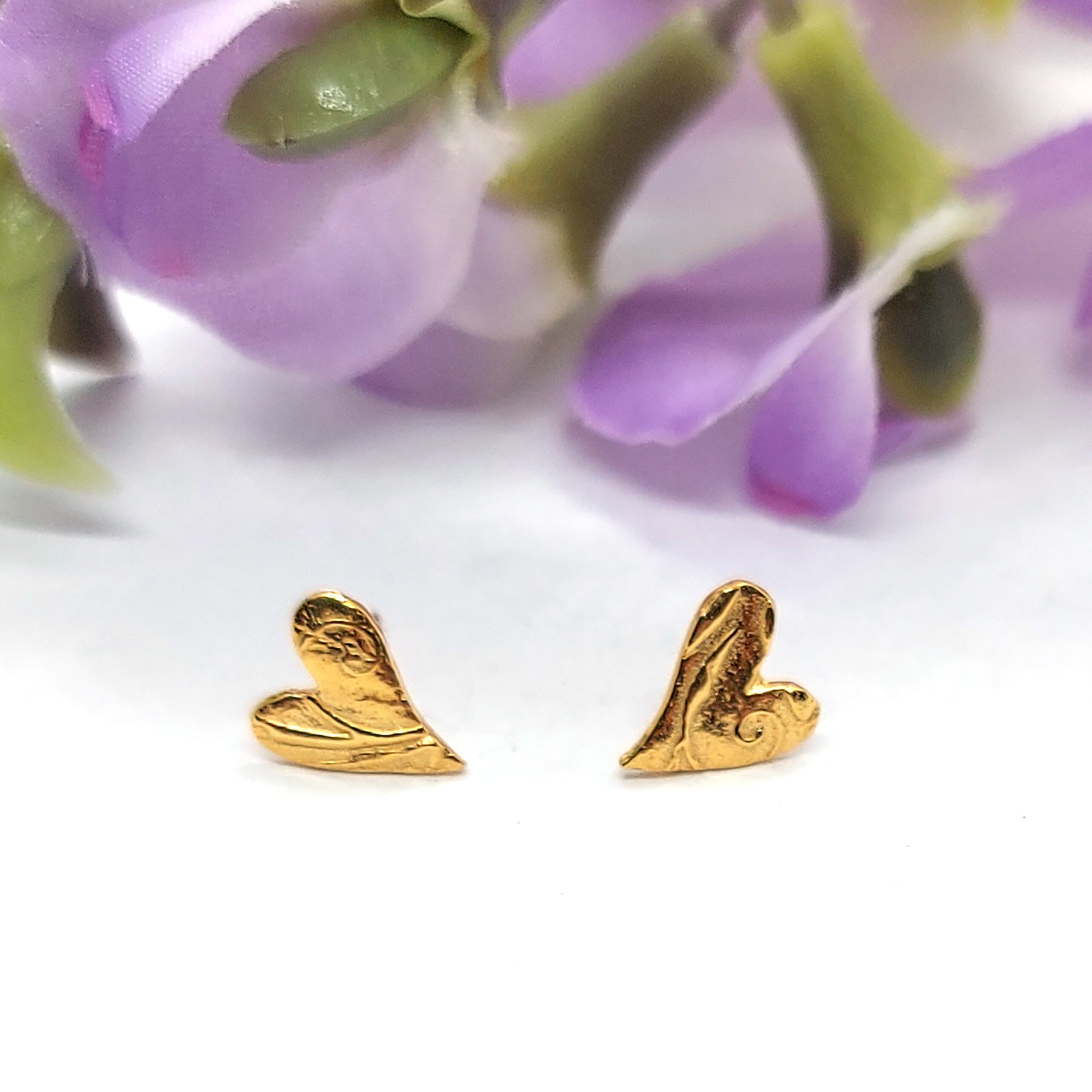 Yellow gold vermeil asymmetrical heart stud earrings with a swirl pattern. Pictured with flowers