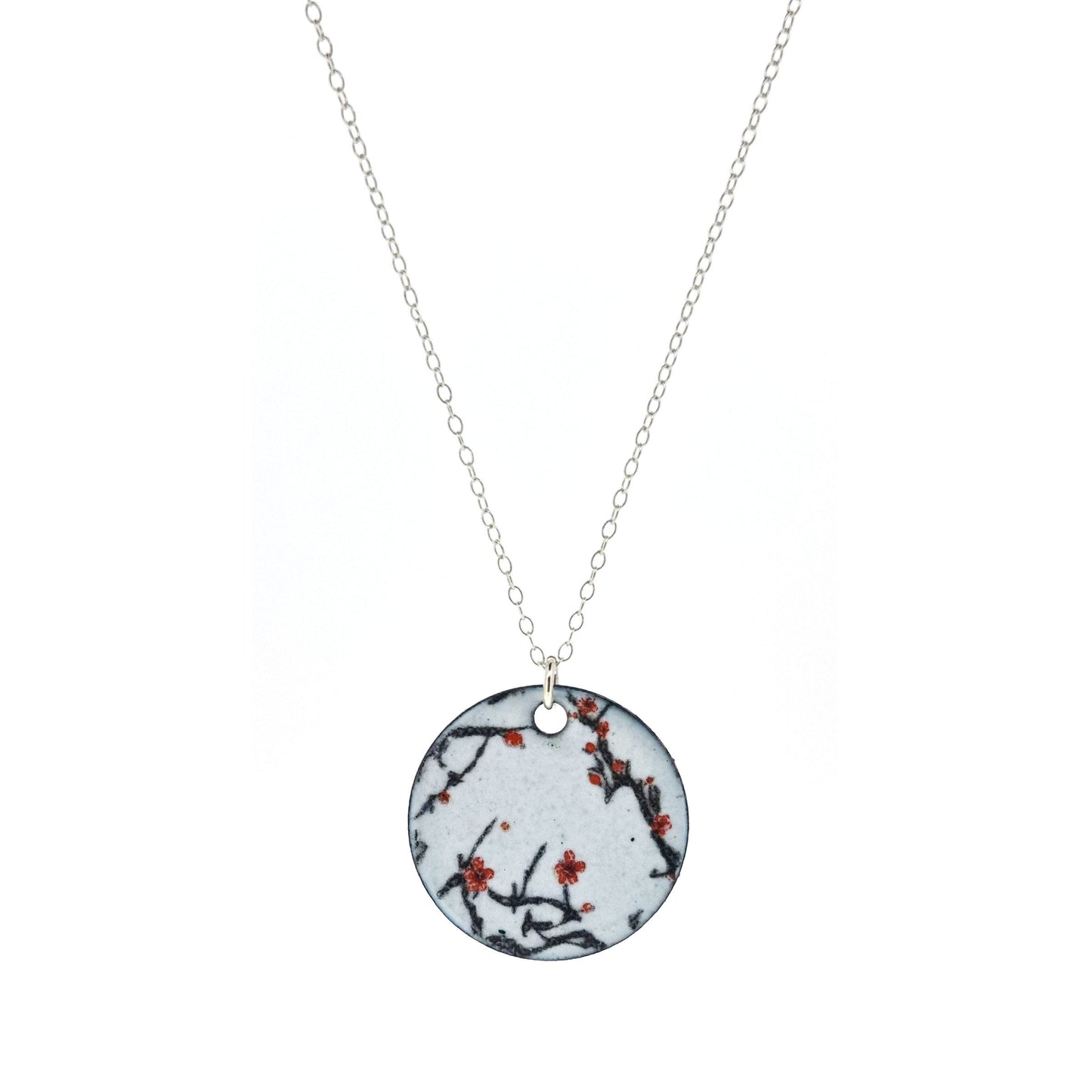 A round enamel pendant hangs from a silver chain. The pendant has a light grey background with branches running across it and red blossom flowers.