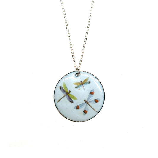A round enamel pendant hangs from a silver chain. The pendant has a light grey background and 3 dragonflies on it.