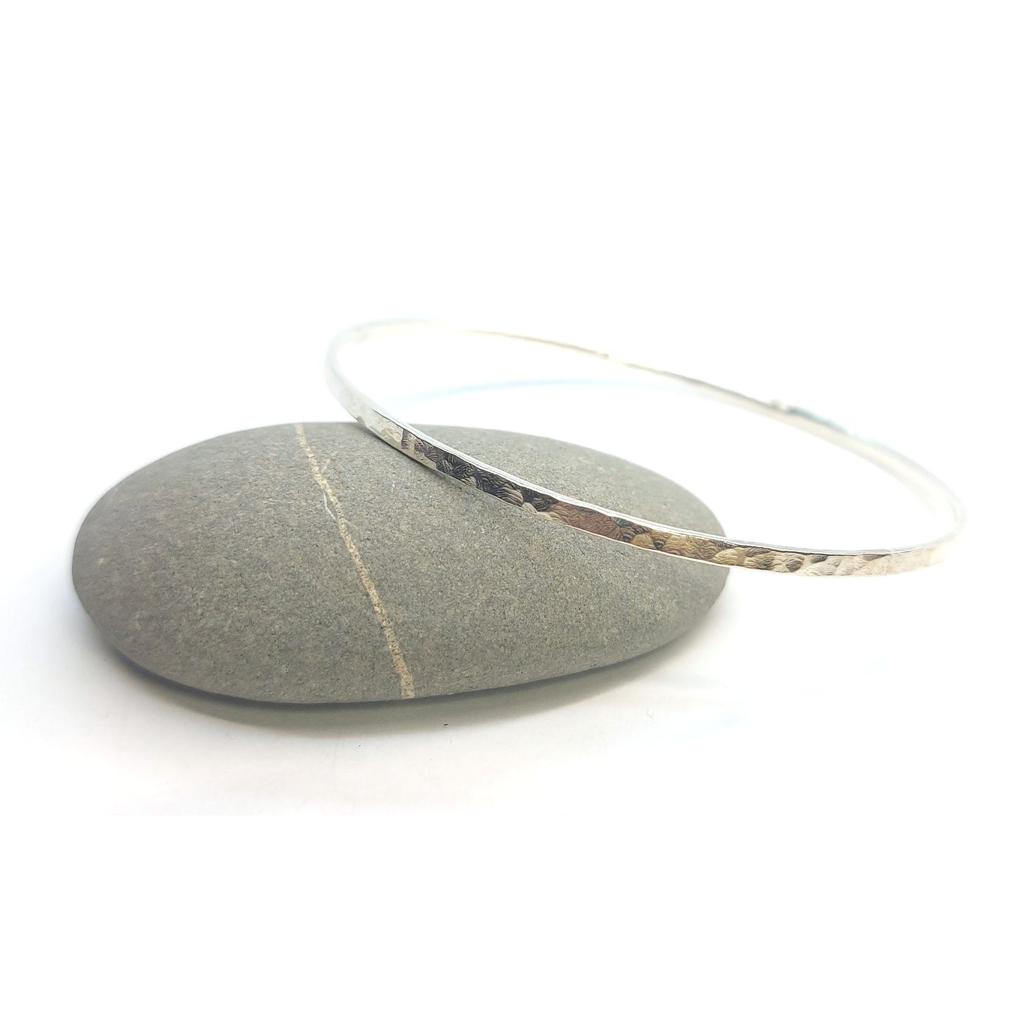 Thin silver hammered stacking slave bangle. Pictured on a pebble.