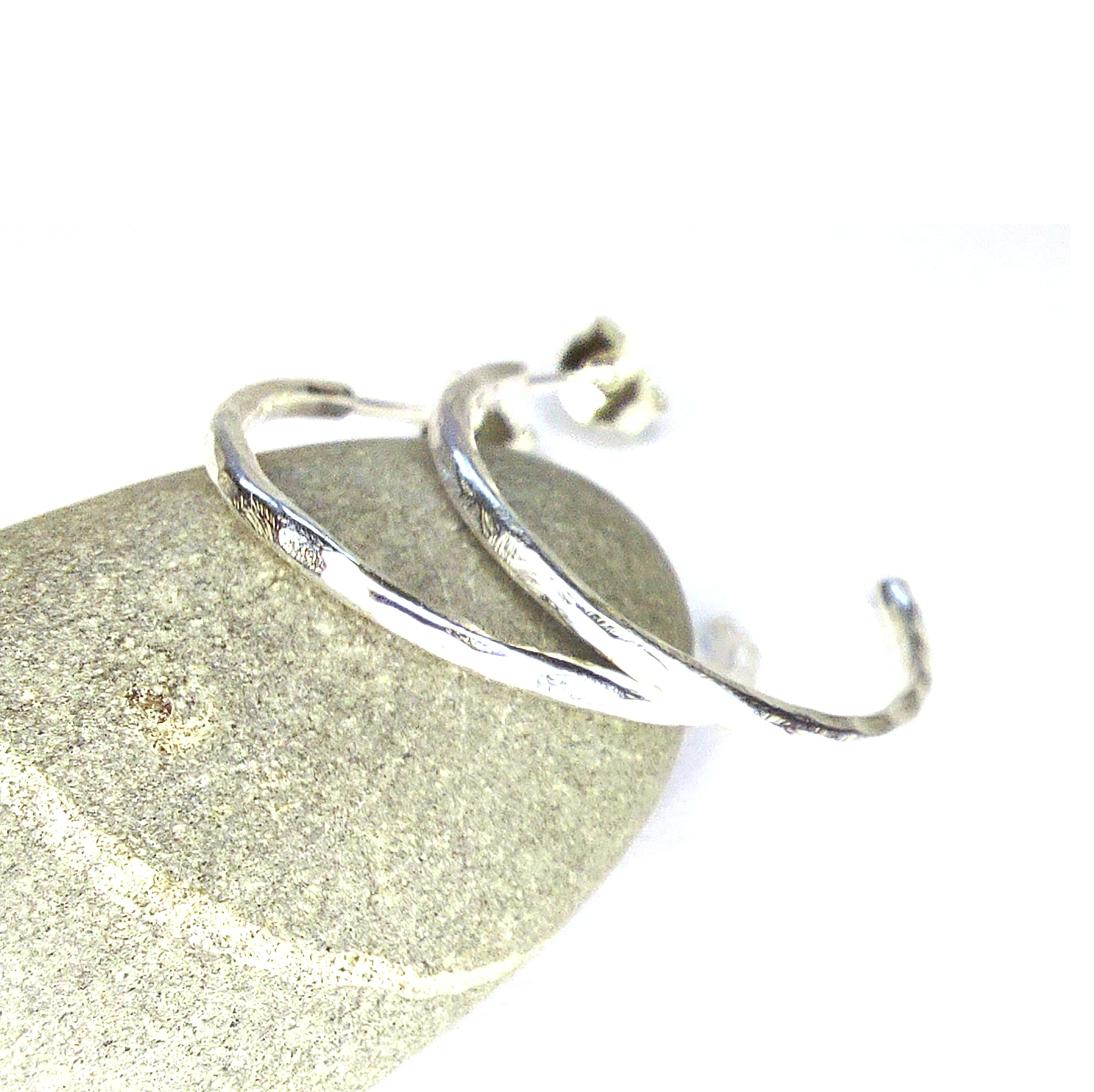 Silver thin hammered hoop earrings - medium. Shown pictured on a pebble.
