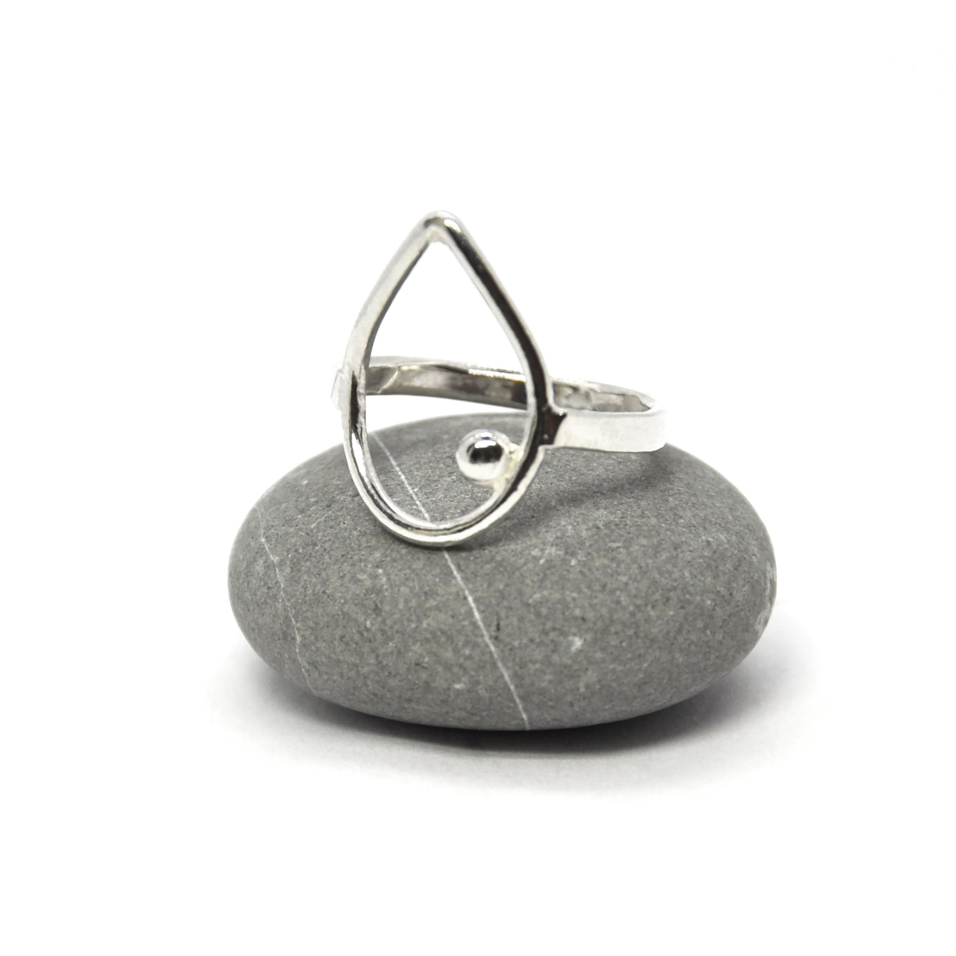 Silver open teardrop shaped ring with off-centre ball. Pictured on a pebble.