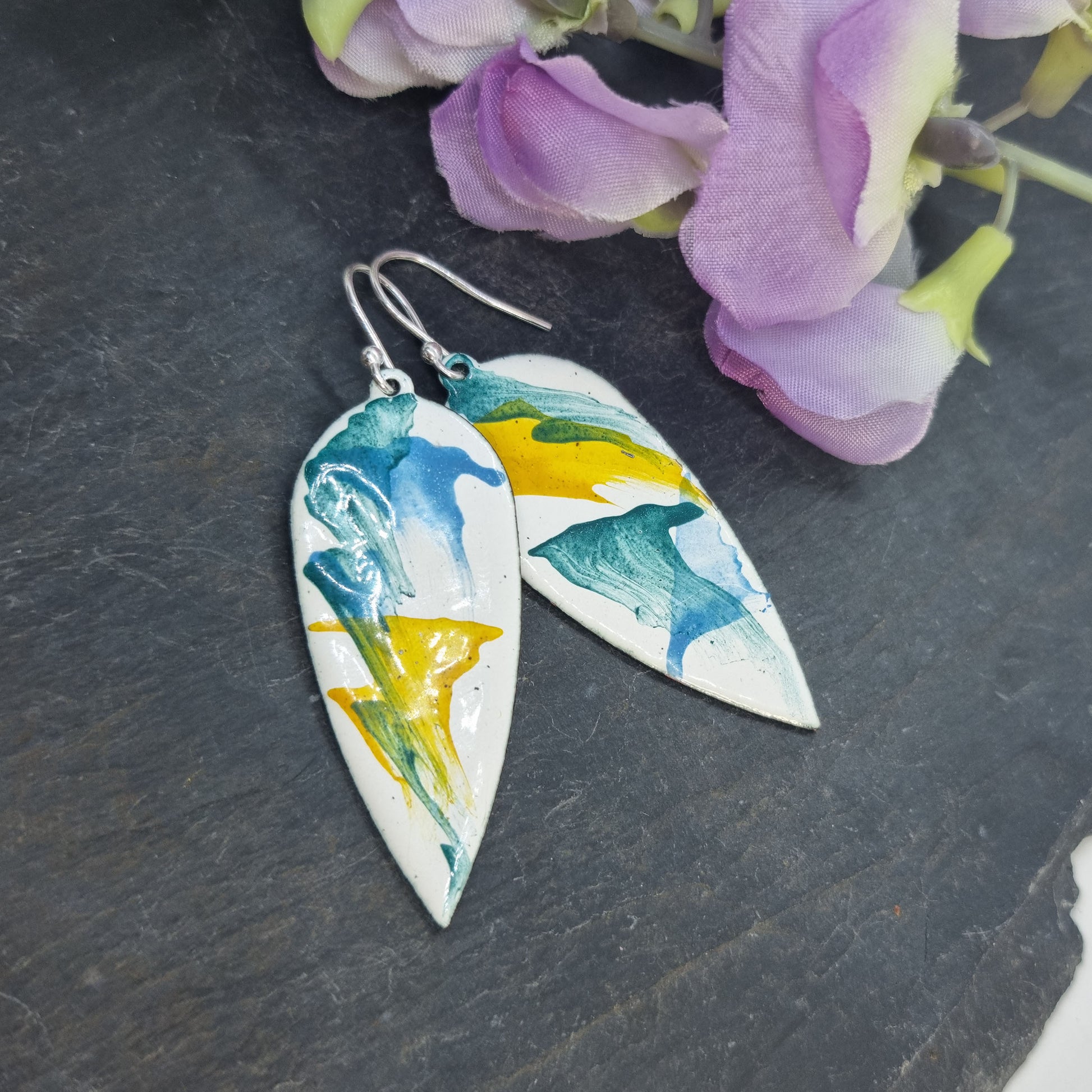 Large teardrop-shaped enamel drop earrings with splashes of green, blue and yellow on a white background - with flowers