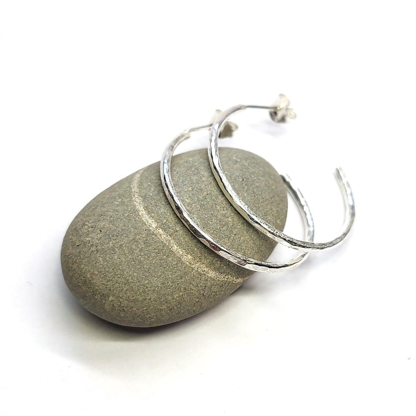 Silver thin hammered hoop earrings - medium. Shown pictured on a pebble.