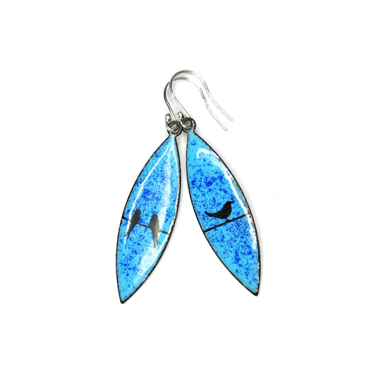 Boat-shaped enamel drop earrings with black bird silhouettes sitting on a wire on a blue background